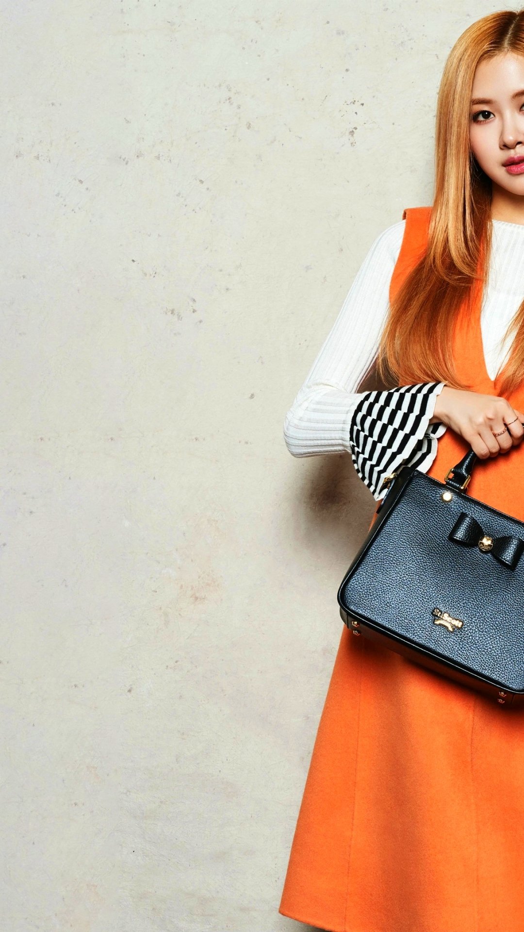 Vertical phone wallpaper of a stylish woman in an orange dress holding a black handbag on the right, textured neutral background, music-inspired BlackPink aesthetic.