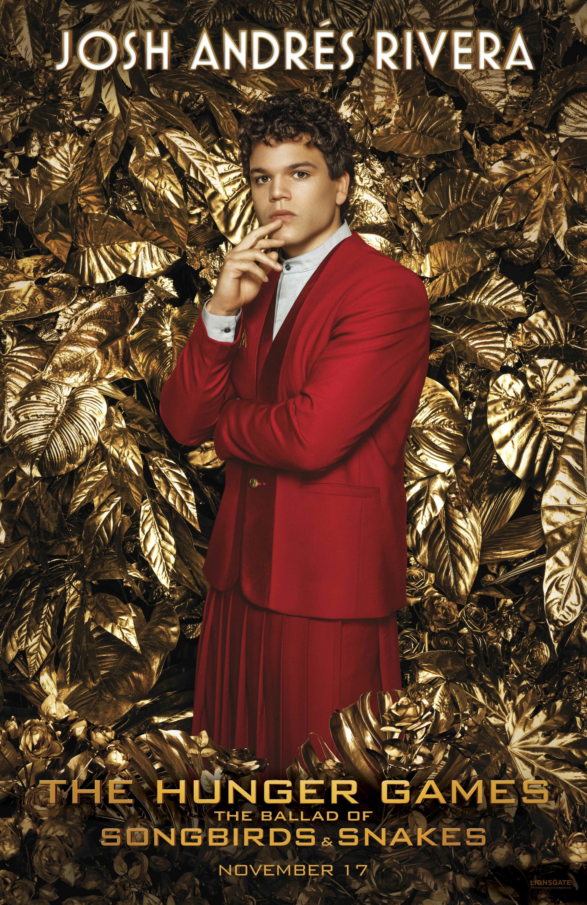 Josh Andres Rivera poses in a striking red outfit against a backdrop of golden leaves in this phone wallpaper for The Hunger Games: The Ballad of Songbirds & Snakes. Release on November 17.