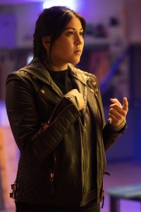 Mobile wallpaper featuring a focused female character from the TV show Echo, portrayed by Alaqua Cox, in a leather jacket against a vibrant neon-lit background.
