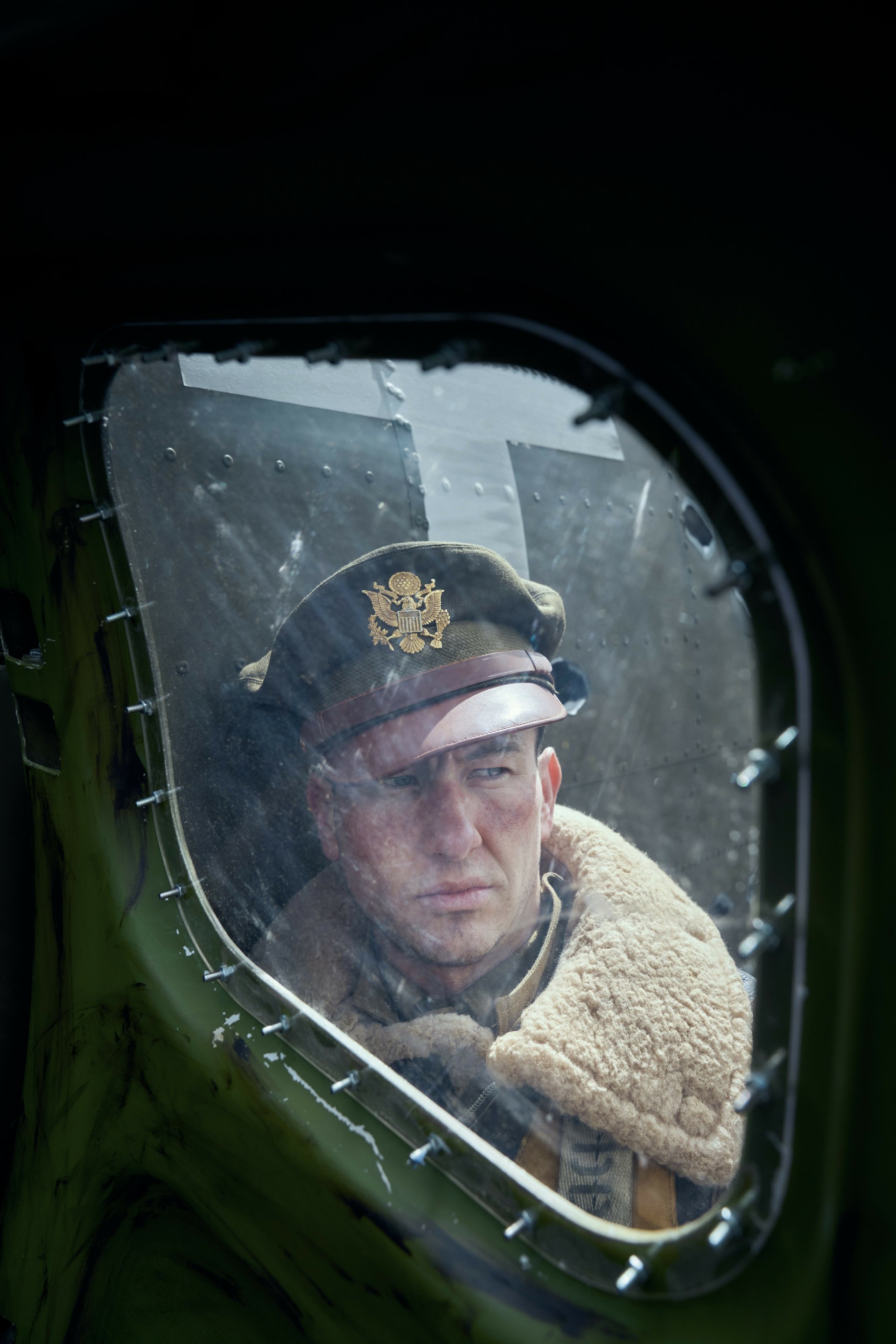 Wallpaper from the TV show Masters of the Air featuring a contemplative military officer looking through an aircraft window.