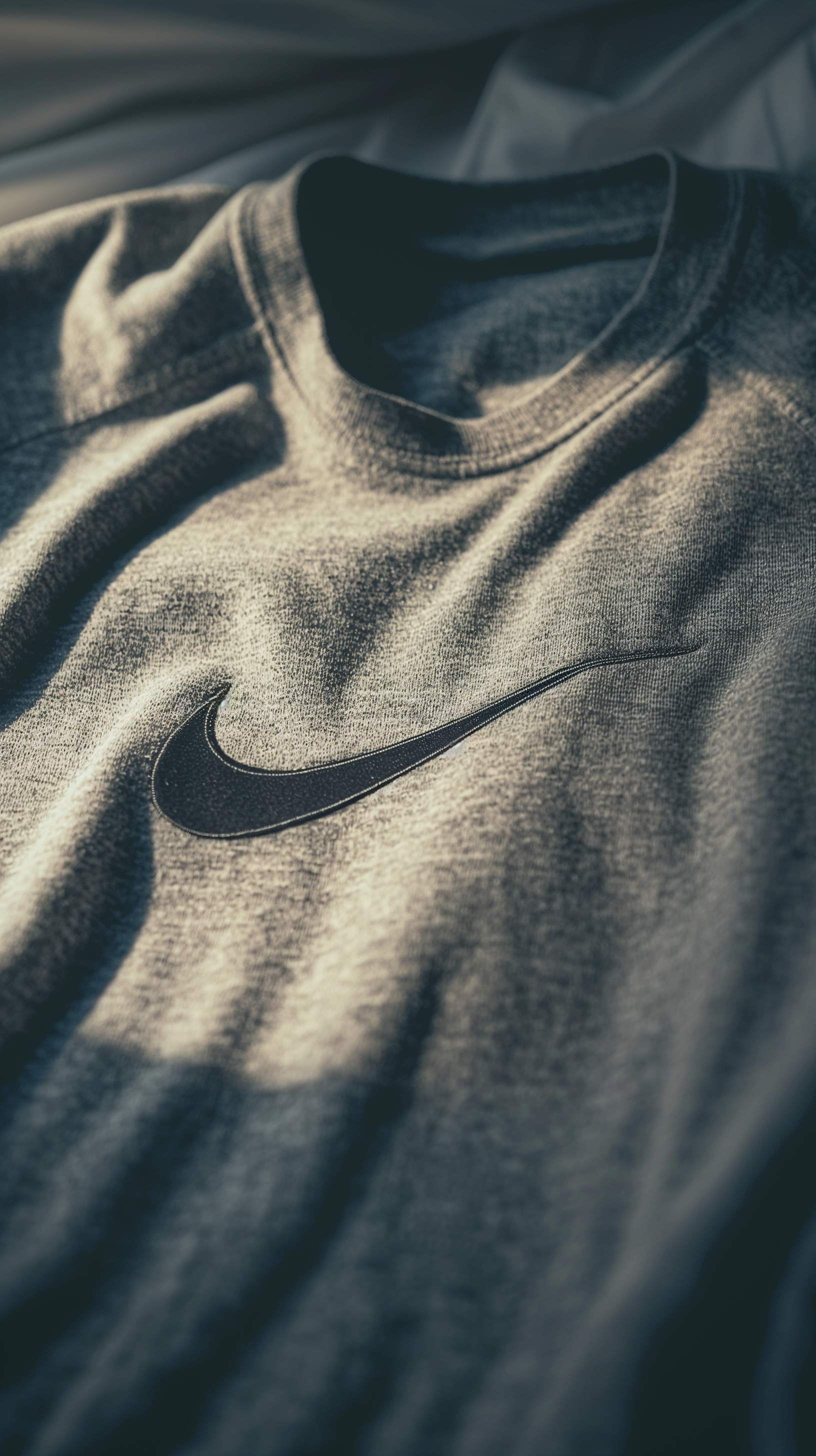 Close-up of a gray Nike t-shirt showcasing the iconic swoosh logo, featuring soft textures and natural lighting. A stylish phone wallpaper option for sports enthusiasts.