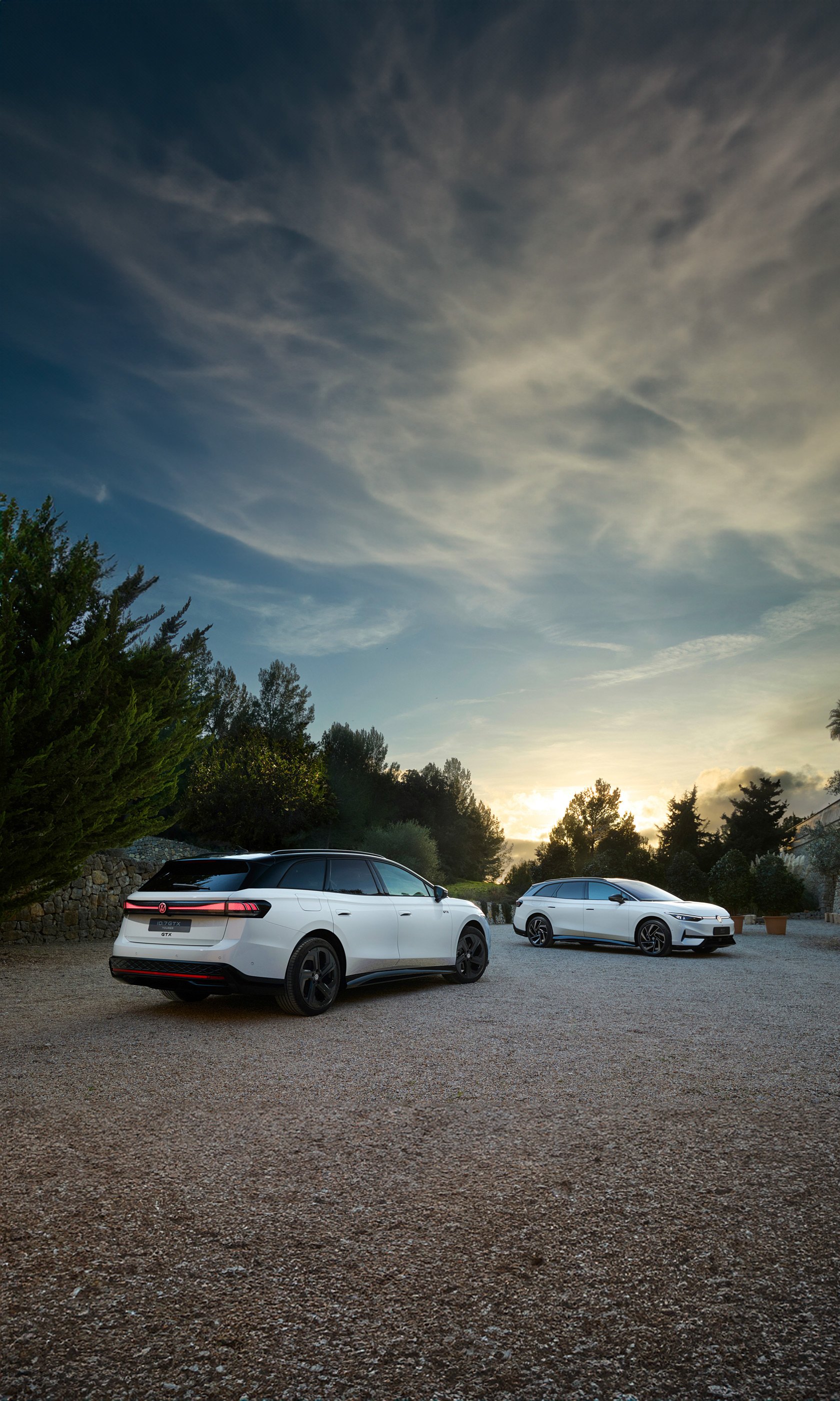 A striking phone wallpaper featuring the Volkswagen ID.7 GTX Tourer parked on a gravel path, framed by lush greenery and a stunning sunset sky.