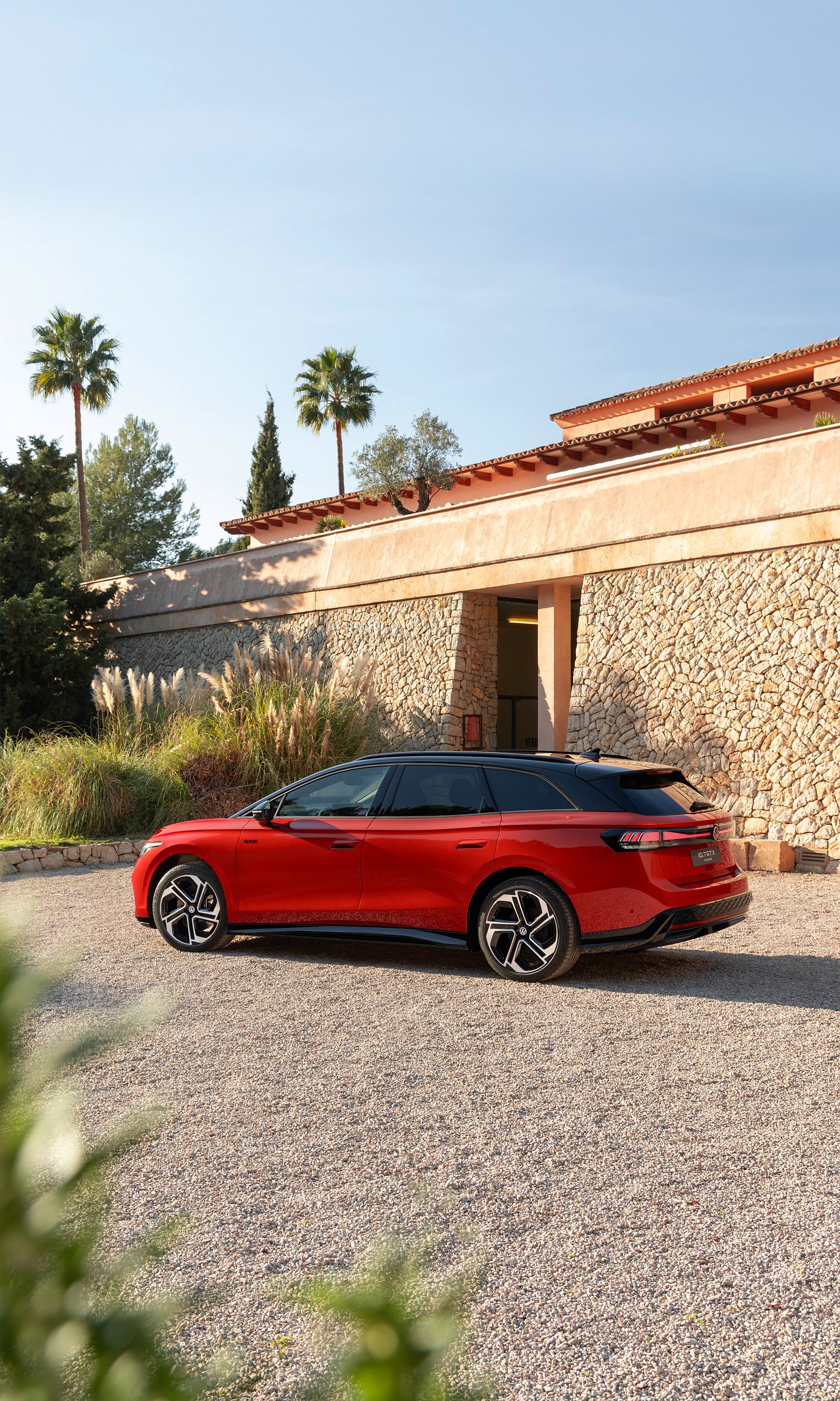 A striking red Volkswagen ID.7 GTX Tourer parked gracefully in a serene landscape, surrounded by greenery and elegant architecture, creating a captivating phone wallpaper.