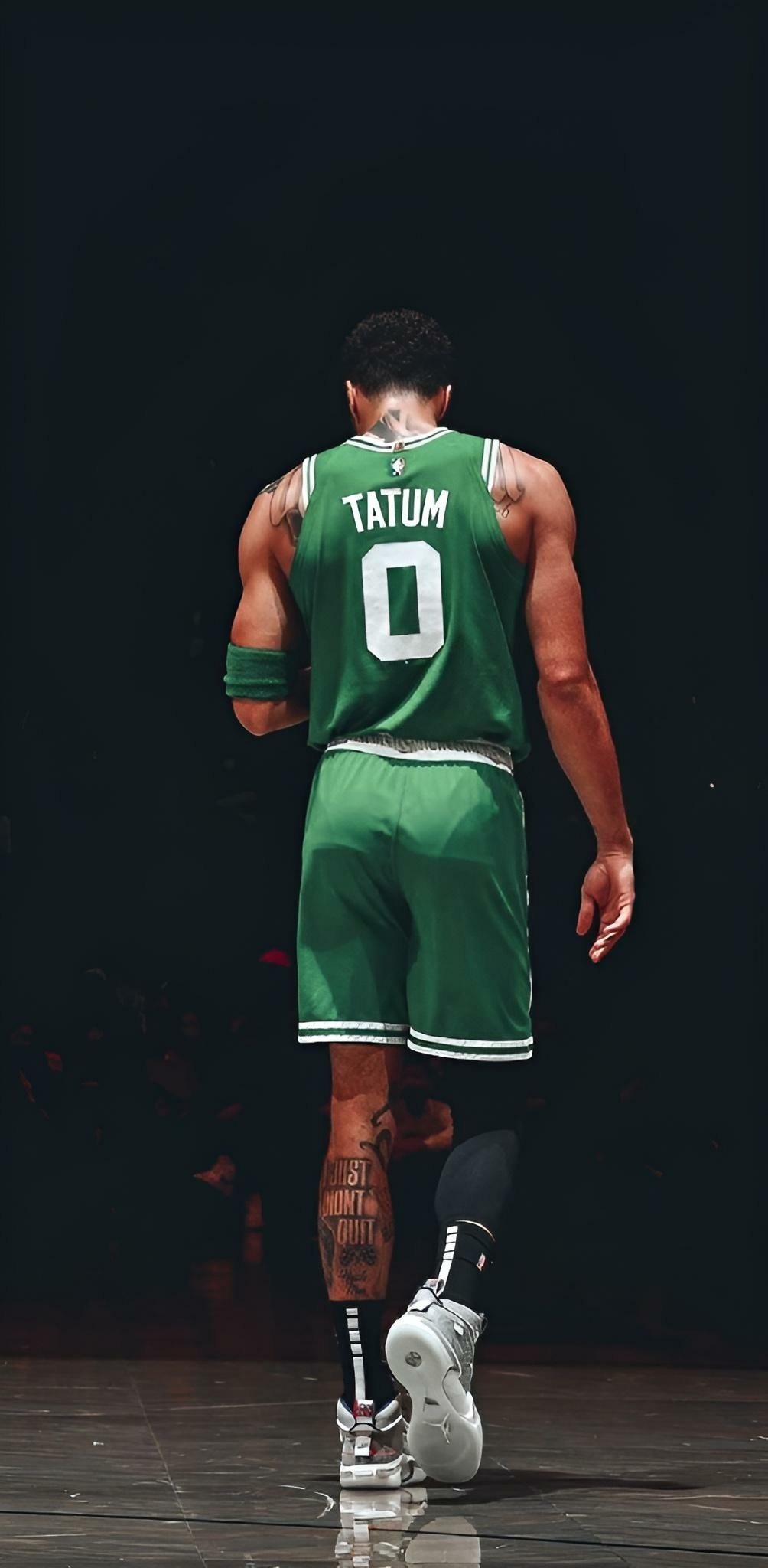 Vertical image of a Boston Celtics player, identified by the jersey name 'Tatum' with the number 0, seen from the back as he stands on a basketball court, designed as a phone wallpaper.
