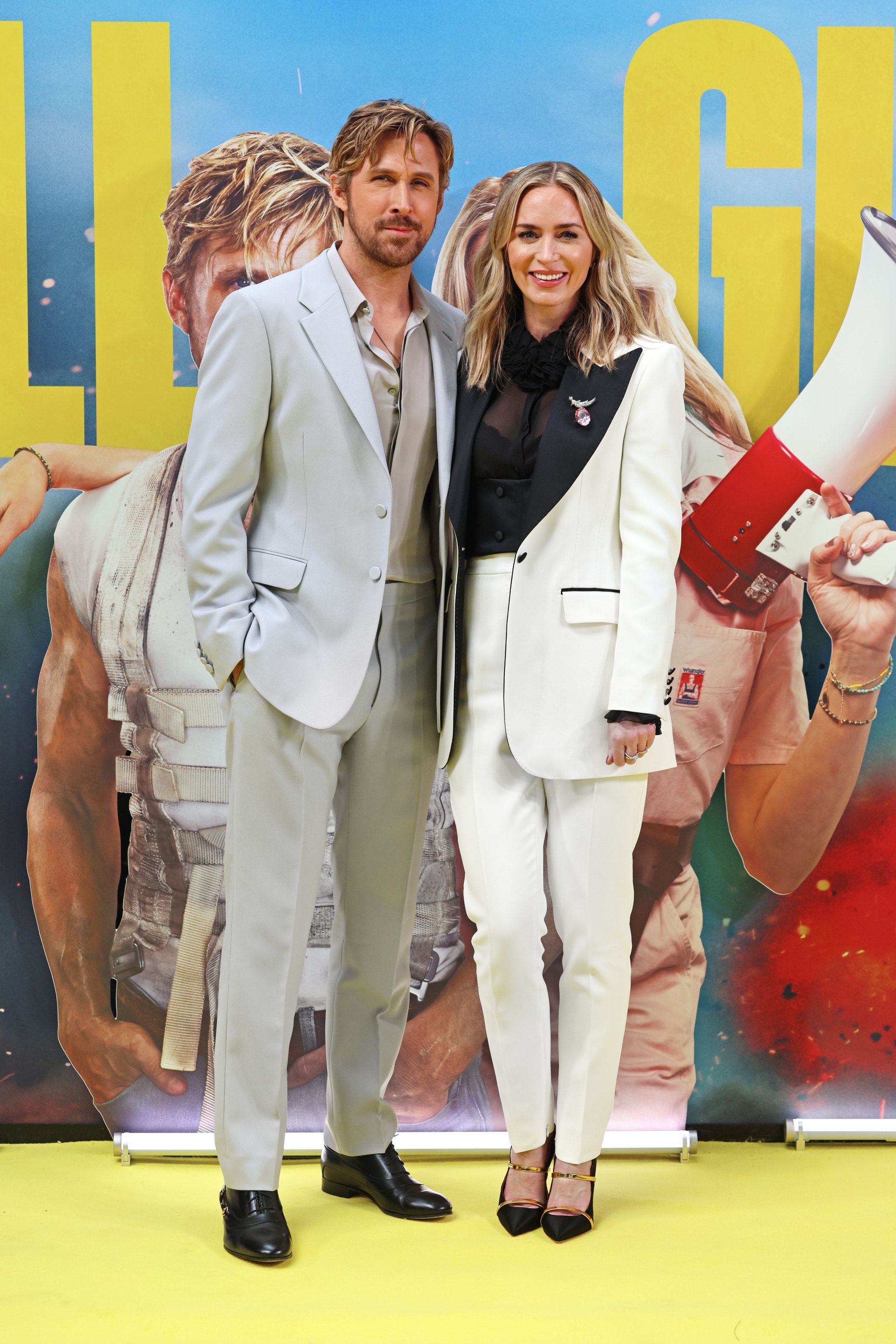 Ryan Gosling and Emily Blunt pose in white outfits at 'The Fall Guy' movie event, making this a vibrant phone wallpaper featuring the stars.