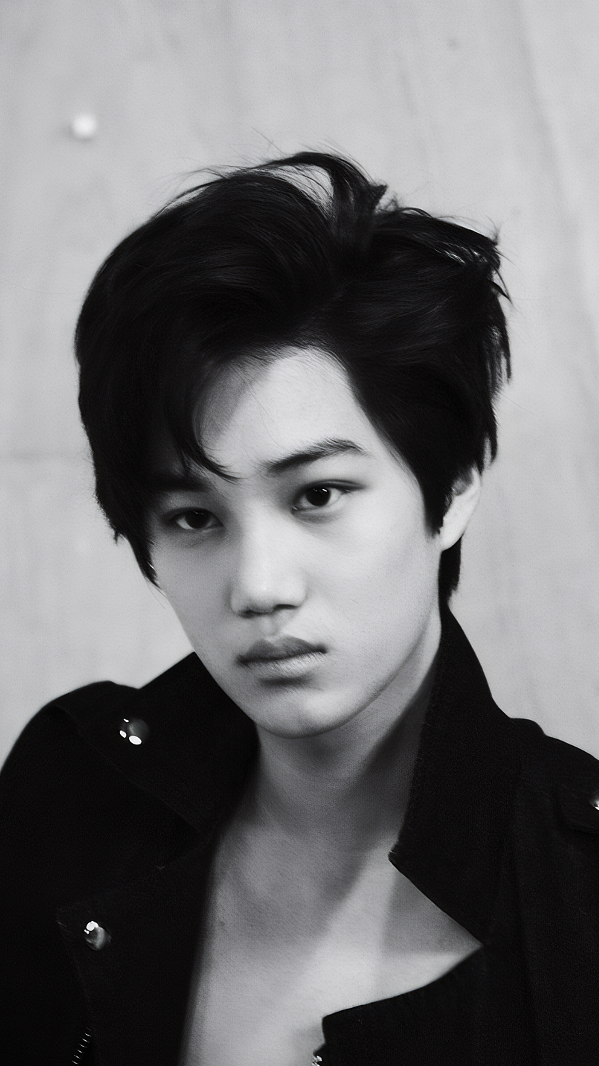 Black and white phone wallpaper of Kai from EXO’s Mama photoshoot, featuring a close-up portrait with tousled hair and an intense gaze, designed for iPhone and Android screens.