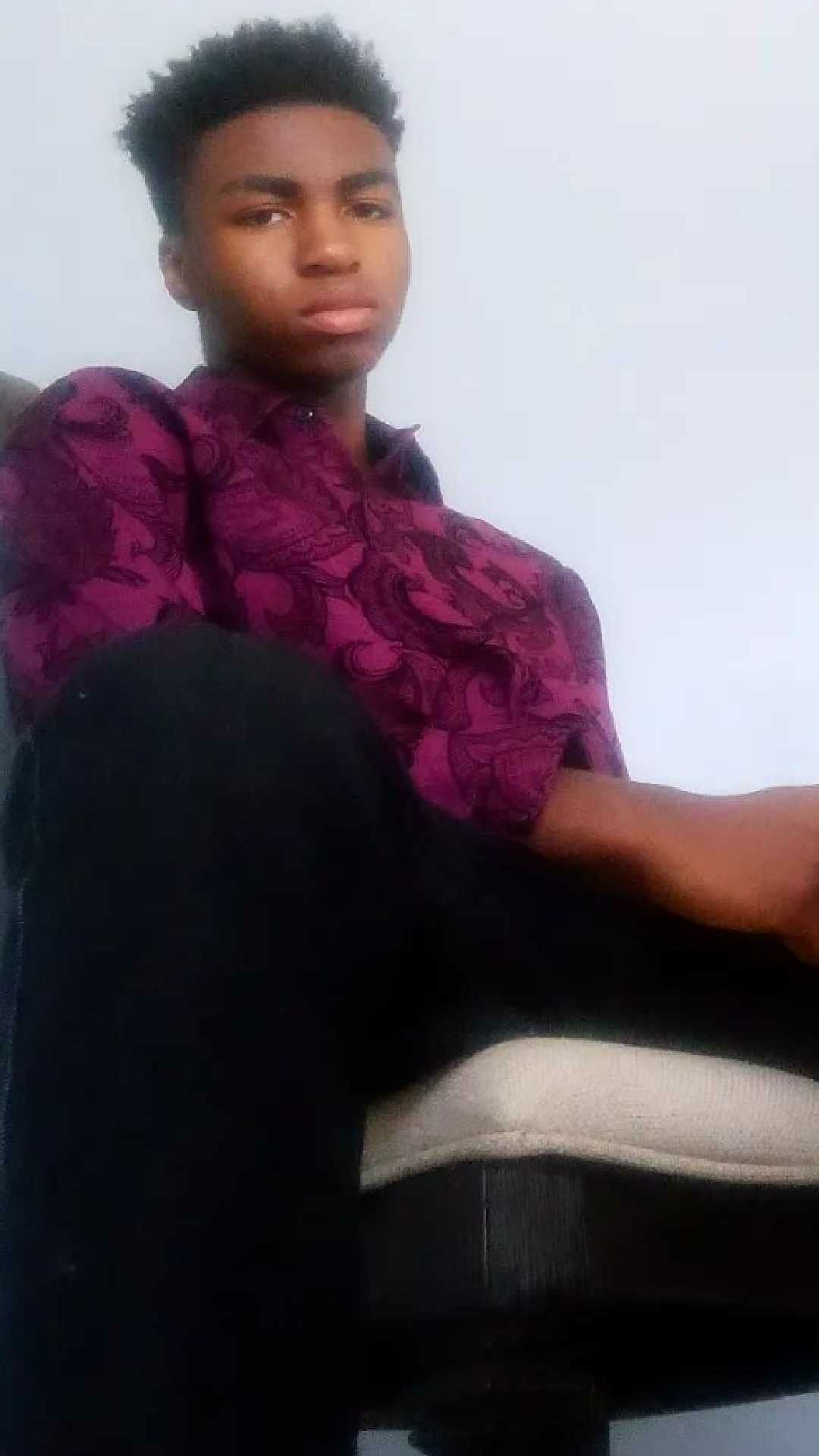 Portrait of Israel McCorkle wearing a purple patterned shirt, sitting confidently against a light background; designed as a fashion phone wallpaper for iPhone and Android.