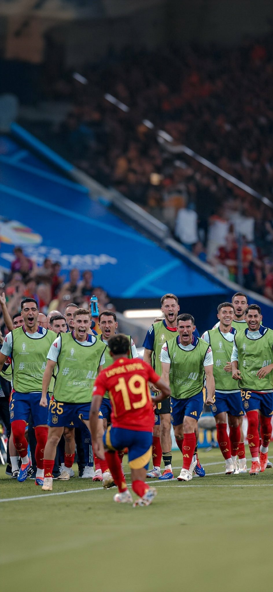 Phone wallpaper featuring the Spain National Football Team's Lamine Yamal in high spirits on the field, celebrating with teammates.