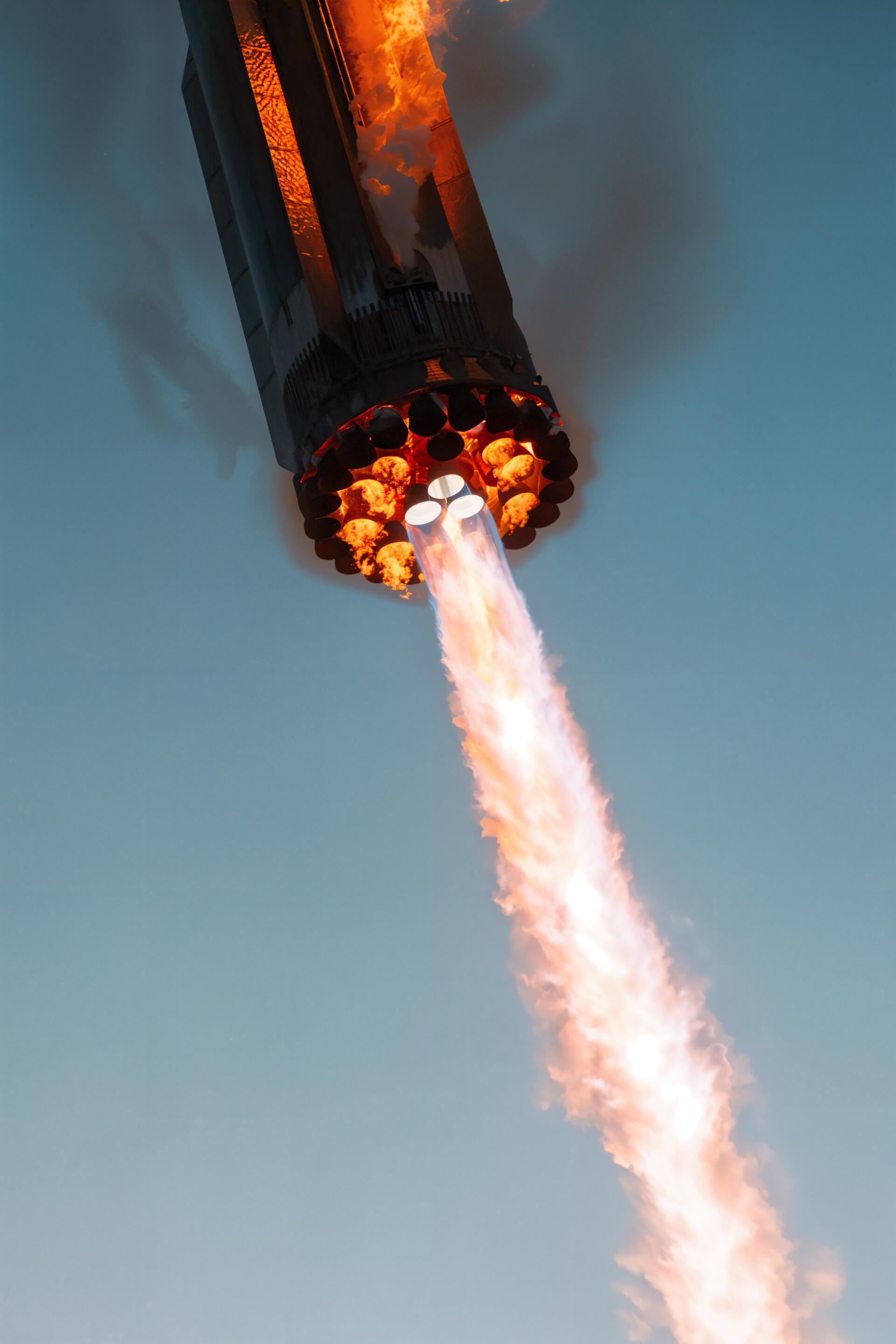 SpaceX Superheavy booster with bright flames from engines during ascent, captured against a clear sky, designed as a dynamic phone wallpaper for iPhone and Android.