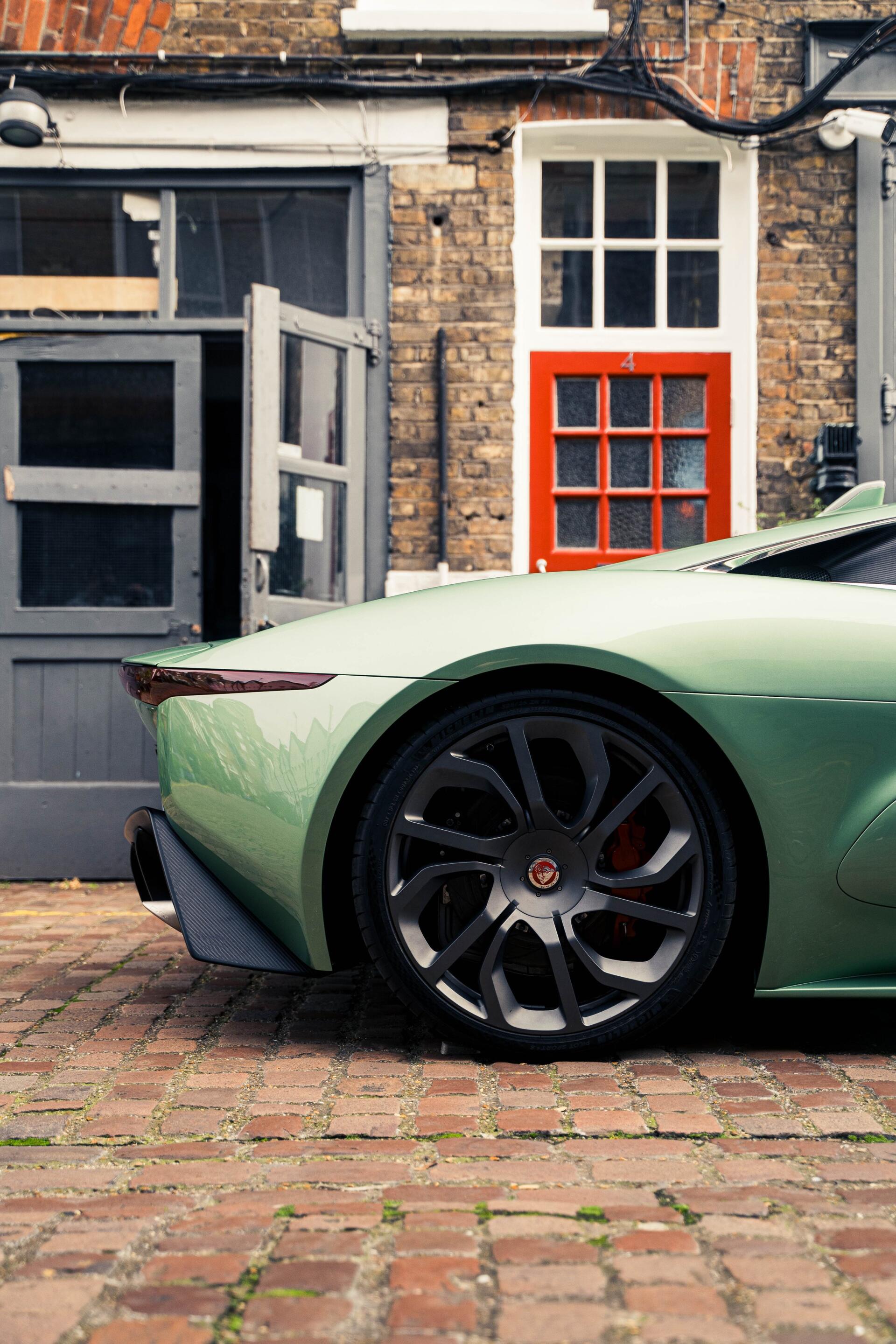 A sleek Jaguar C-X75 is parked against a rustic brick backdrop, showcasing its elegant curves and distinctive design, making it an eye-catching phone wallpaper.