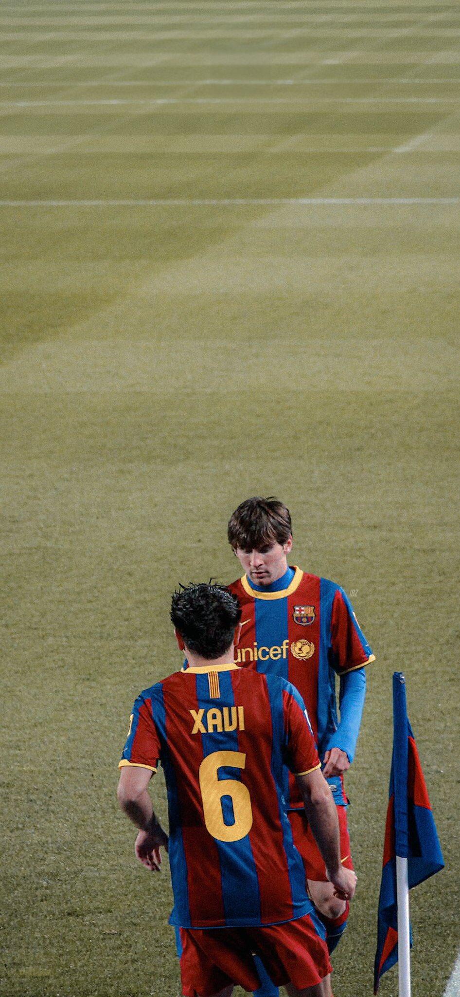 Xavi Hernández and Lionel Messi in FC Barcelona jerseys share a moment on the pitch, embodying the spirit of teamwork and soccer passion in this dynamic phone wallpaper.