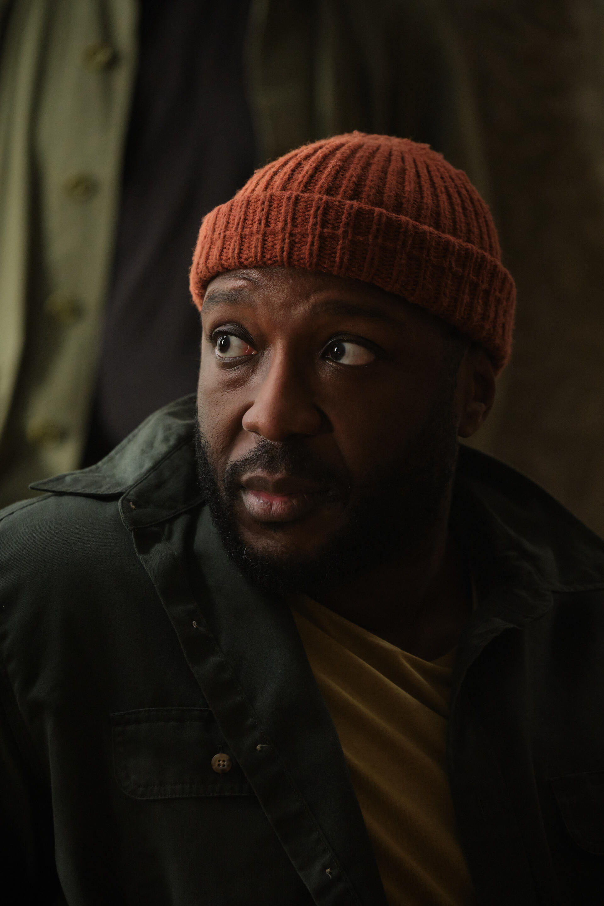 A captivating phone wallpaper from the TV show The Crow Girl (2025), featuring Raphael Sowole with an intense expression, wearing an orange beanie and dark jacket.