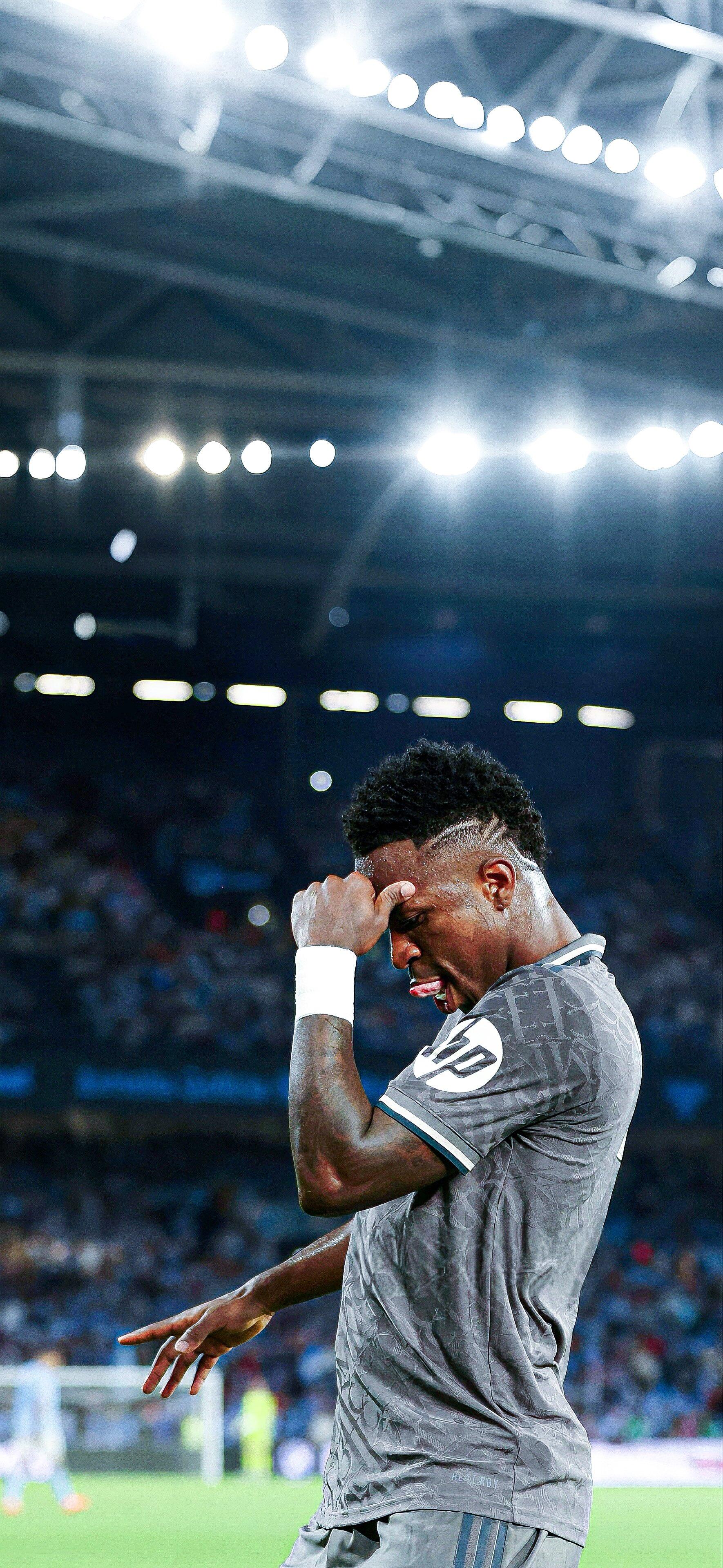 Vinícius Júnior of Real Madrid C.F. shows emotion on the field during a match, illuminated by stadium lights, capturing the intensity of soccer. A dynamic phone wallpaper.