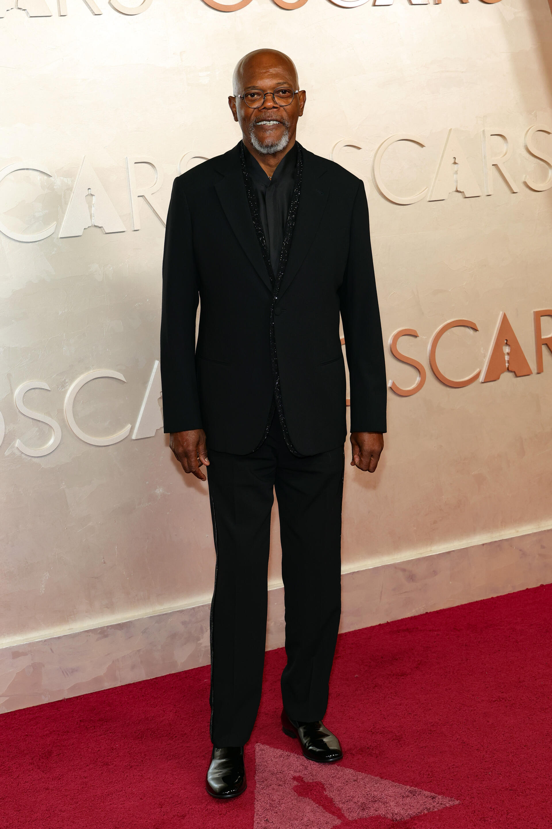 Samuel L. Jackson stands confidently on the red carpet at the Academy Awards, dressed in a sleek black suit, capturing the elegance of this prestigious event.