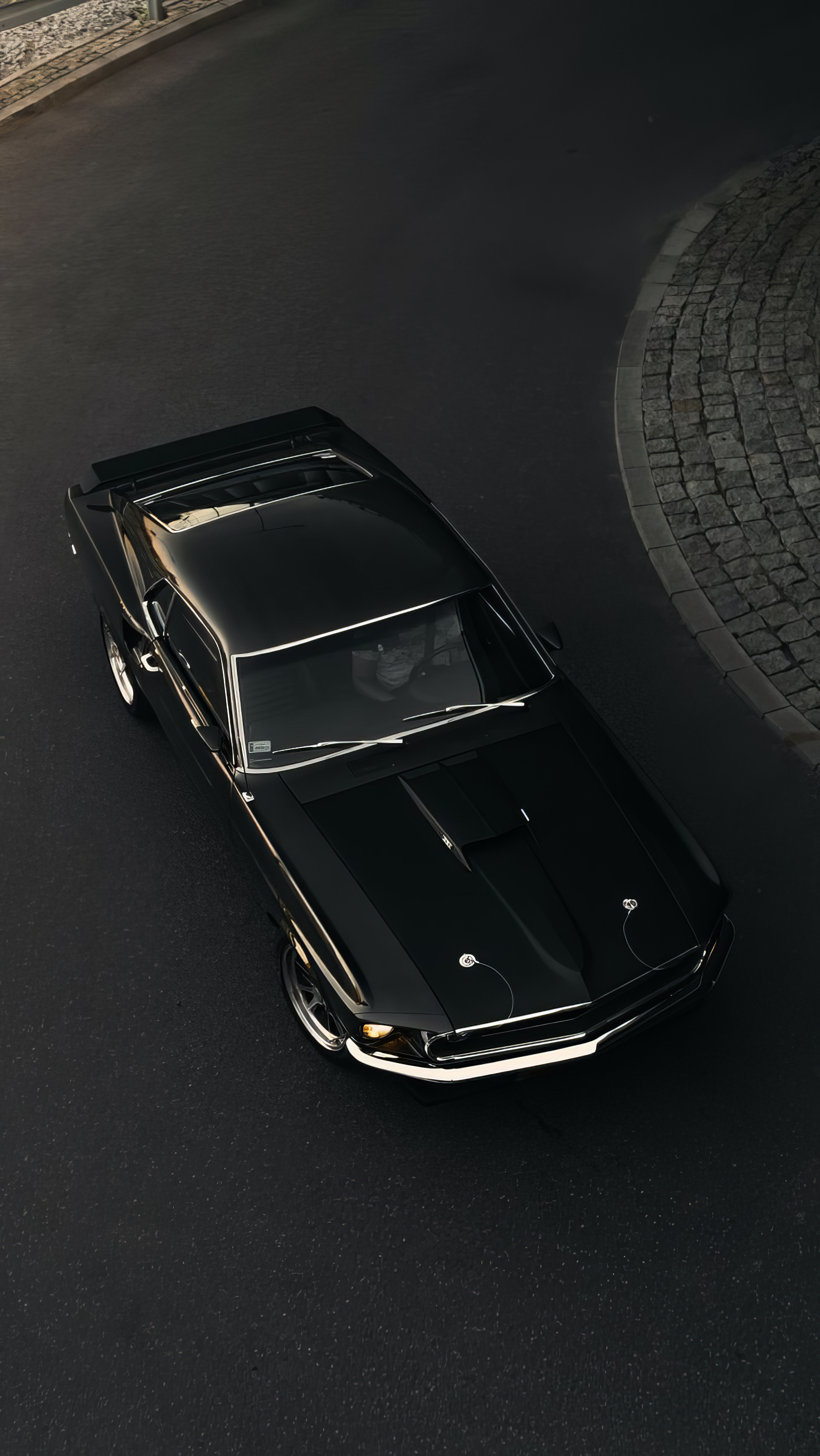 A sleek black Ford Mustang is captured from above, showcasing its stylish design as it sits on a winding cobblestone street, making a striking phone wallpaper.