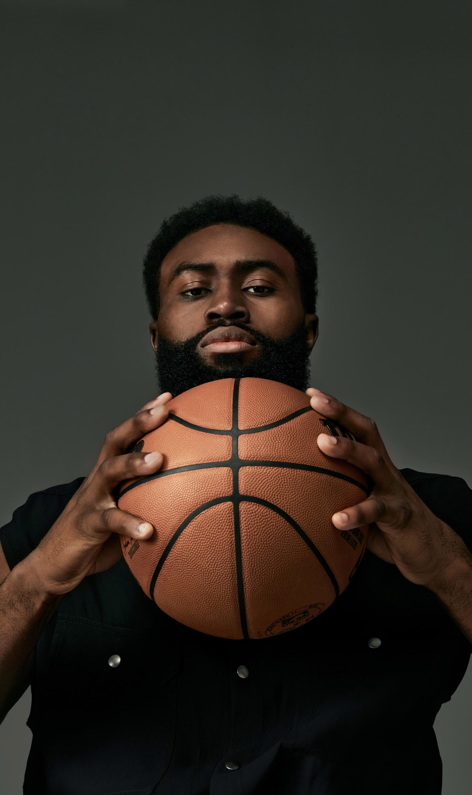Portrait of NBA player Jaylen Brown holding a basketball against a dark background, designed as a phone wallpaper for iPhones and Android devices.