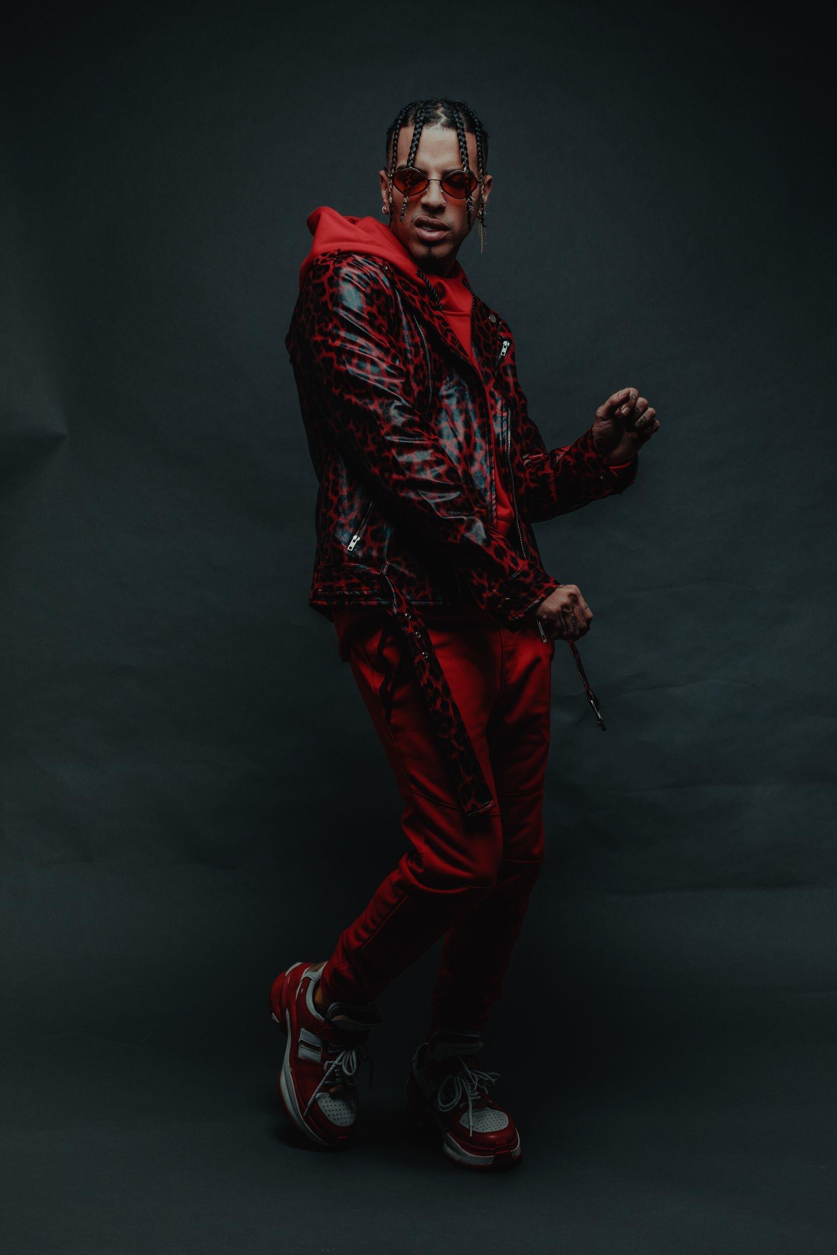 Phone wallpaper featuring music artist Rauw Alejandro in a dark red outfit and sunglasses, posing against a black background, compatible with iPhones and Android devices.