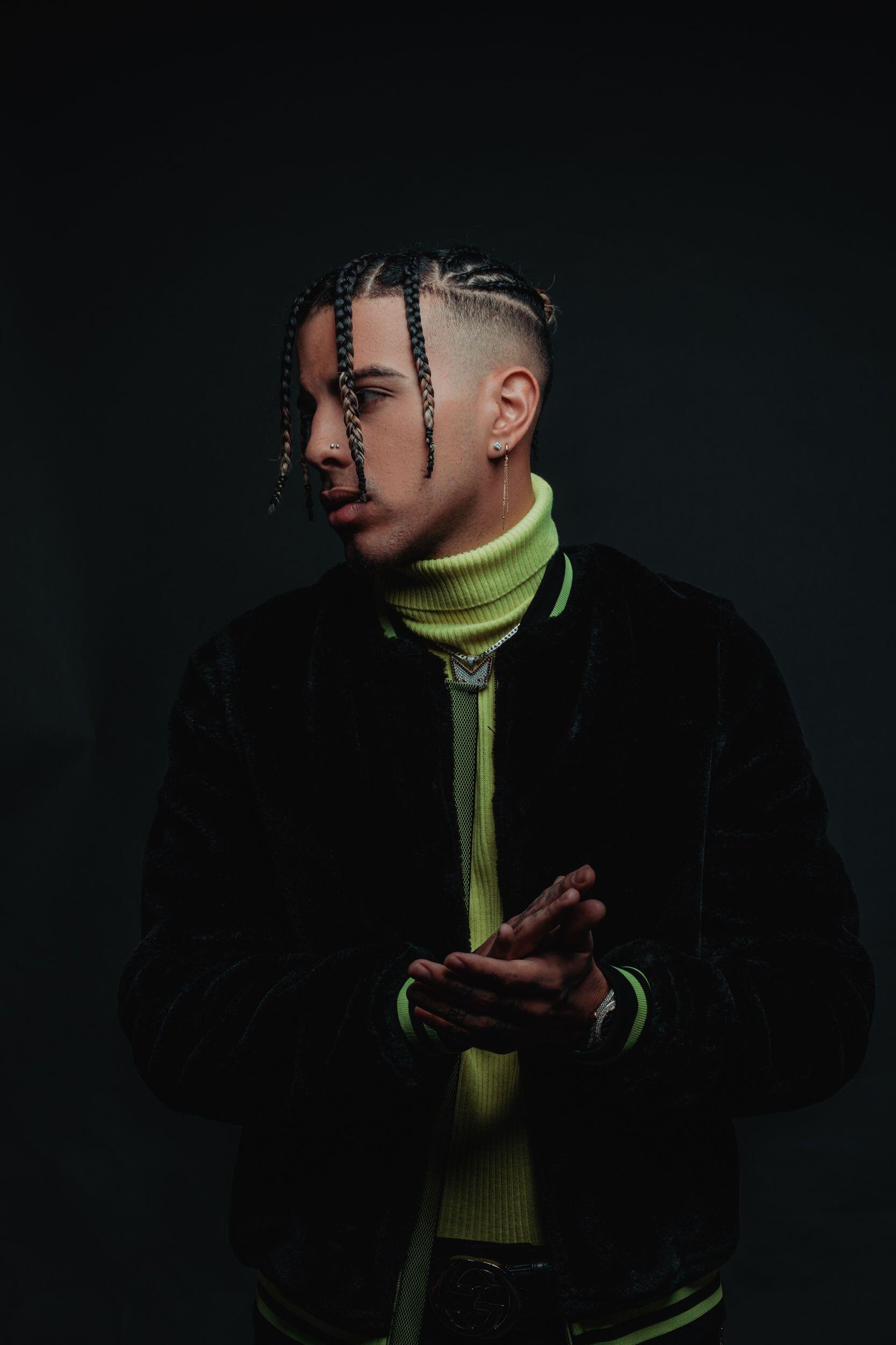 Phone wallpaper featuring music artist Rauw Alejandro in a profile pose, wearing a neon green turtleneck and dark jacket against a black background. Compatible with iPhones and Android phones.