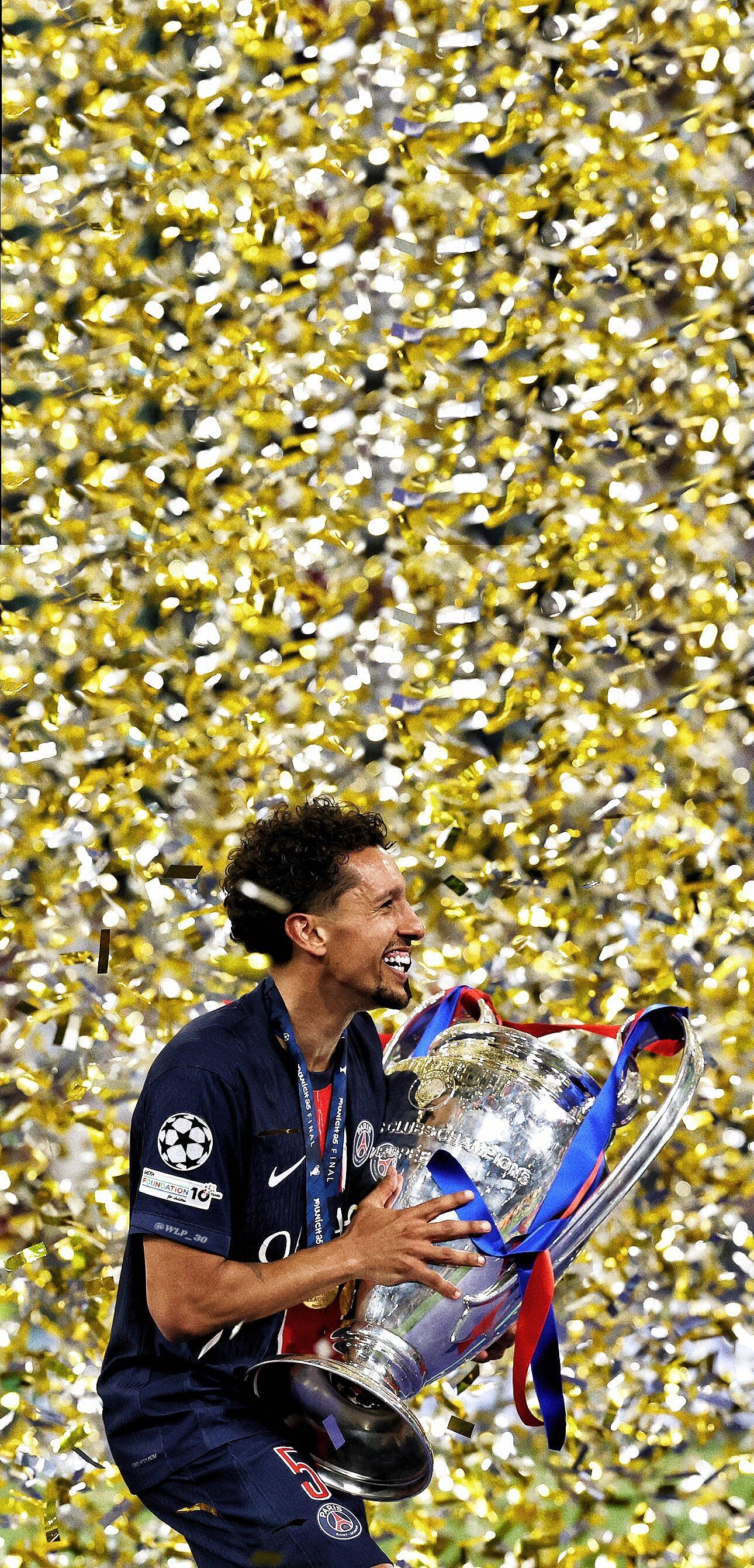 Marcos Aoás Corrêa of Paris Saint-Germain F.C. celebrates with the UEFA Champions League trophy amid falling gold confetti in this dynamic soccer phone wallpaper.