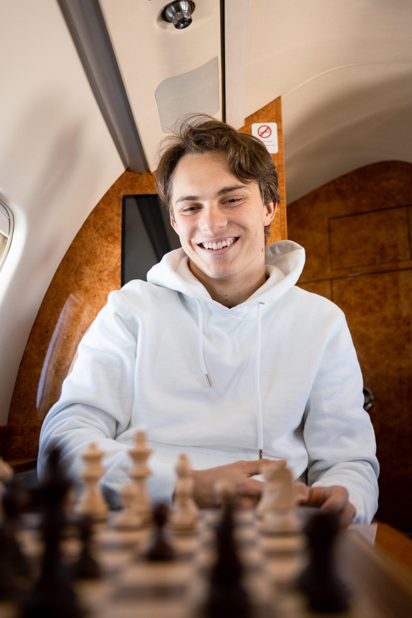 Phone wallpaper featuring Oscar Piastri smiling and playing chess inside a private jet, designed for use on iPhones and Android phones.