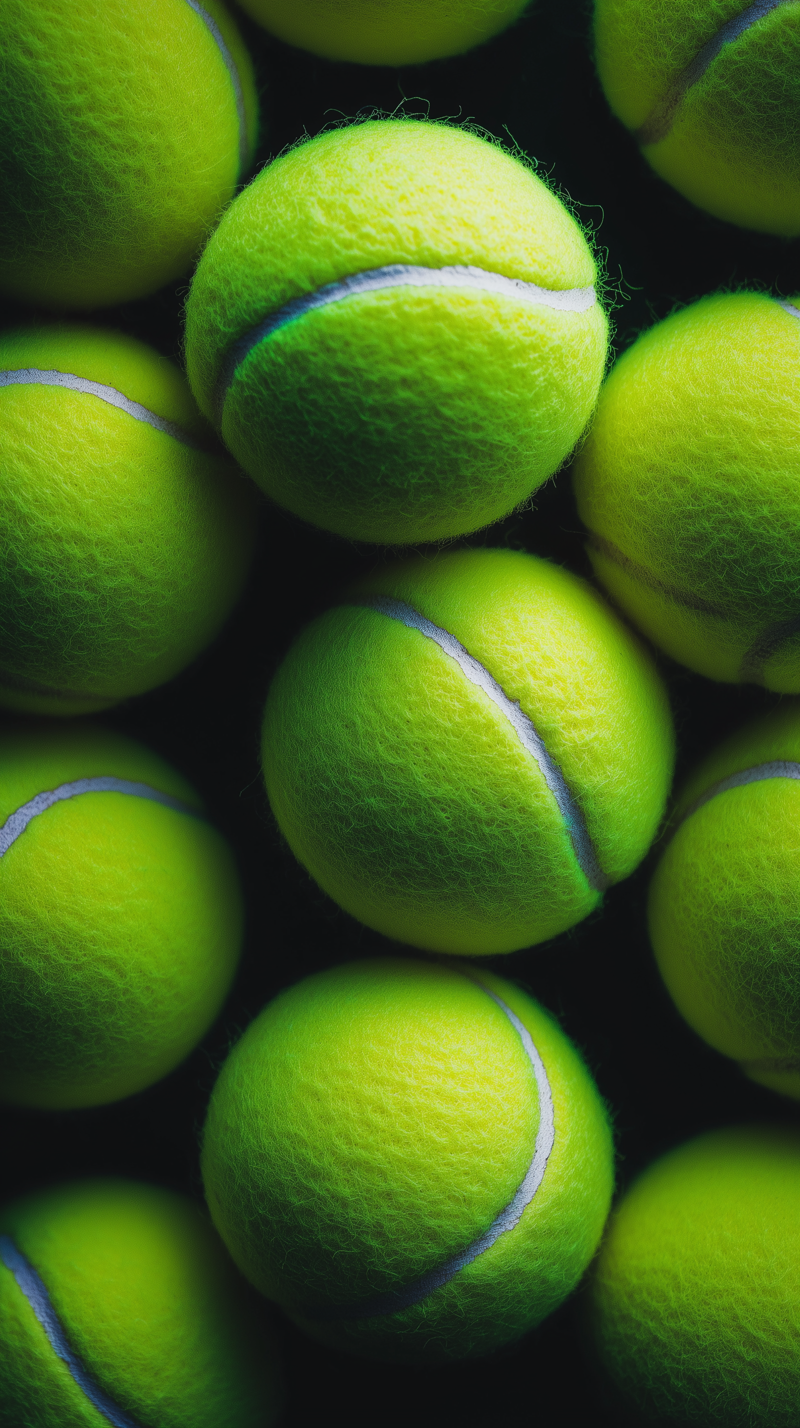 Close-up of vibrant green tennis balls against a dark background, displayed as a vertical phone wallpaper for iPhones and Android devices with a sporty theme.