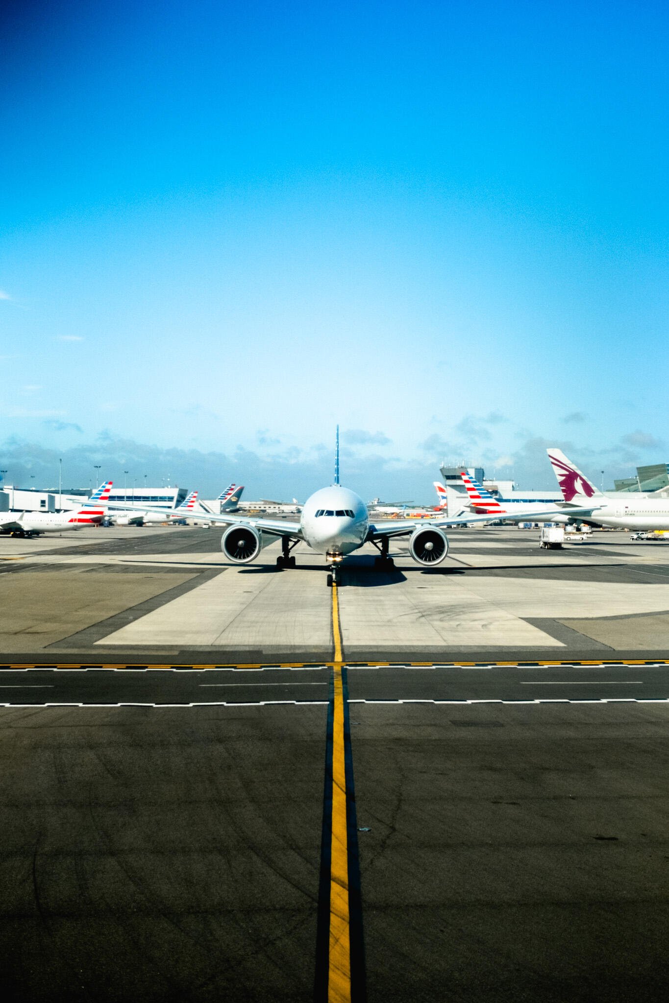 Phone wallpaper showing a front view of an airplane on a runway at a busy USA airport under a clear blue sky, compatible with iPhone and Android screens.