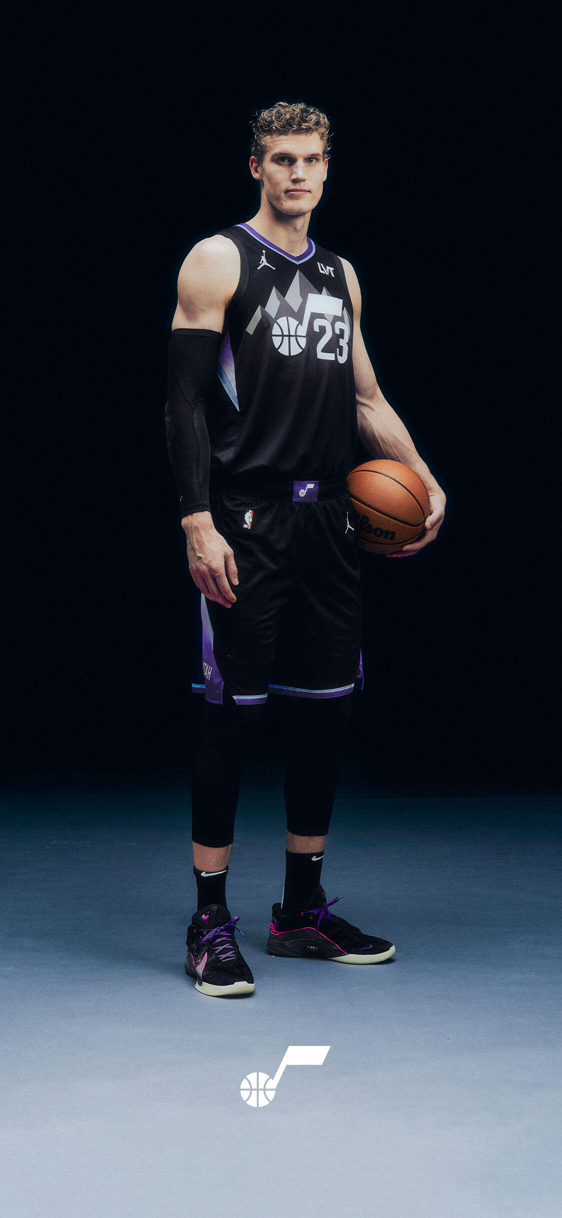 Phone wallpaper of an NBA Utah Jazz player in a black #23 uniform holding a basketball, full-body shot against a dark background with the Jazz logo at the bottom.