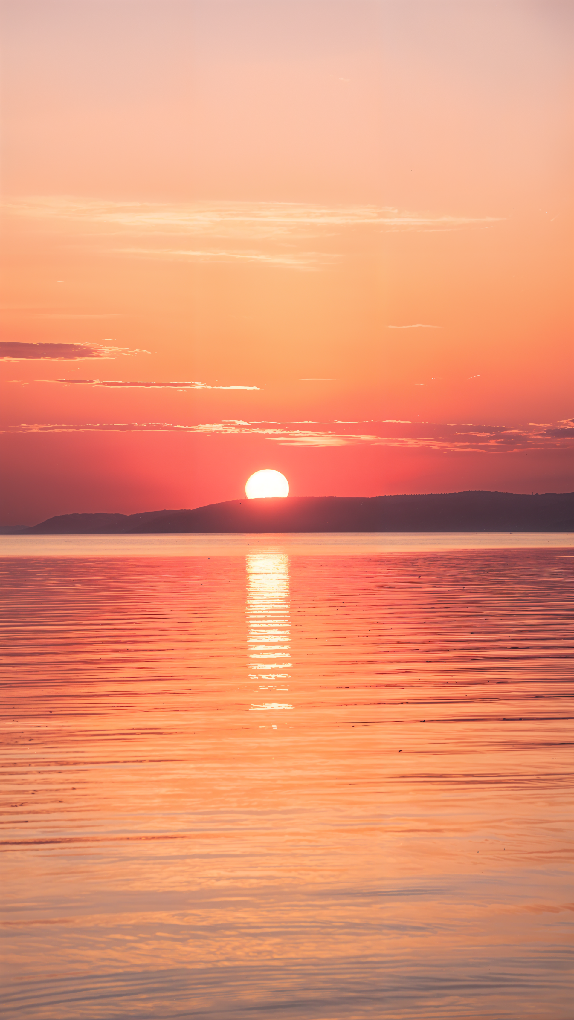 Vertical iPhone wallpaper of a pink-orange sunrise over calm water, the sun touching a distant horizon with a glowing reflection on the rippled sea.