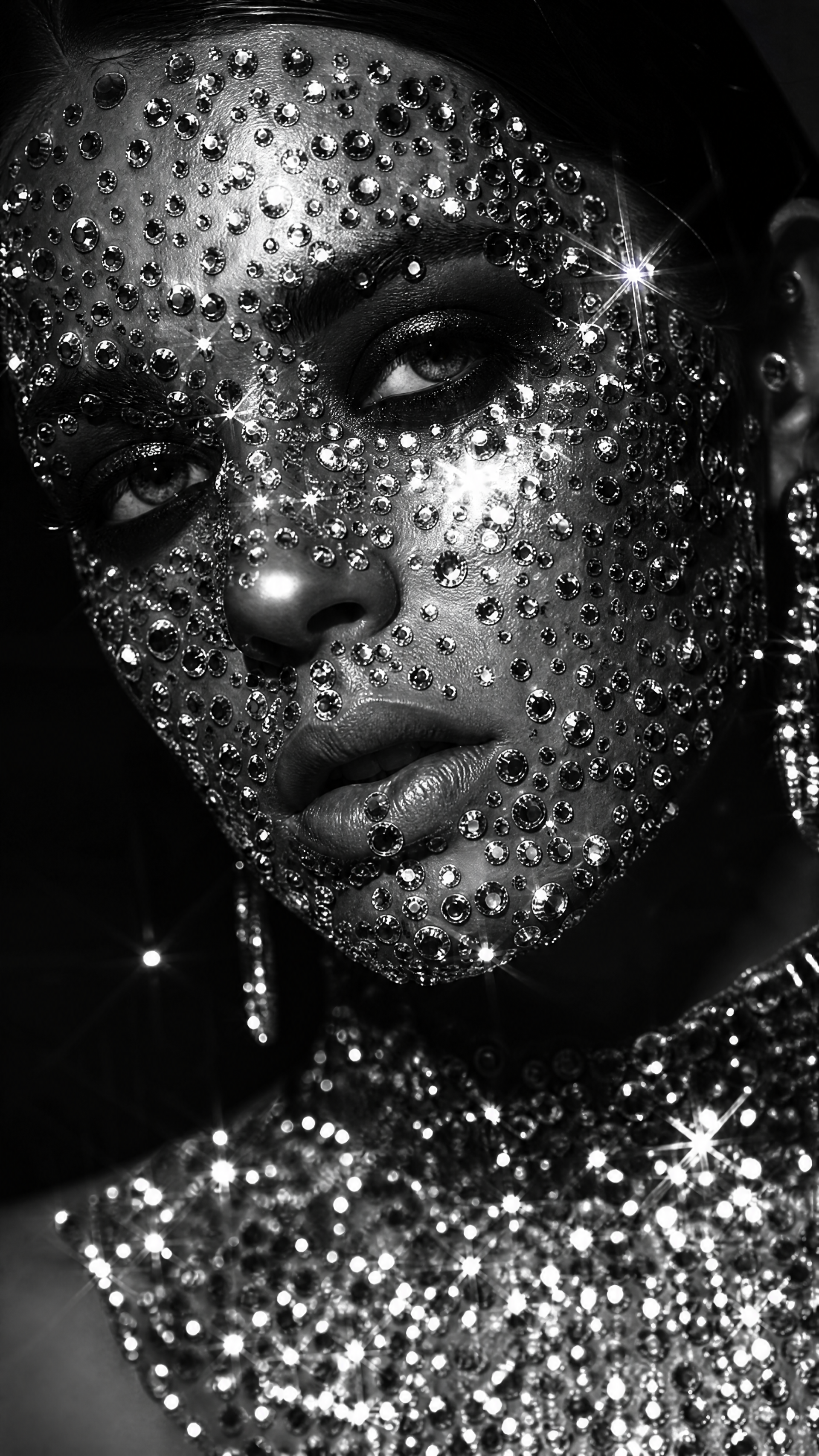 Black-and-white close-up of a bedazzled face encrusted with rhinestones and sparkling jewels; high-contrast glam portrait for an iPhone wallpaper.