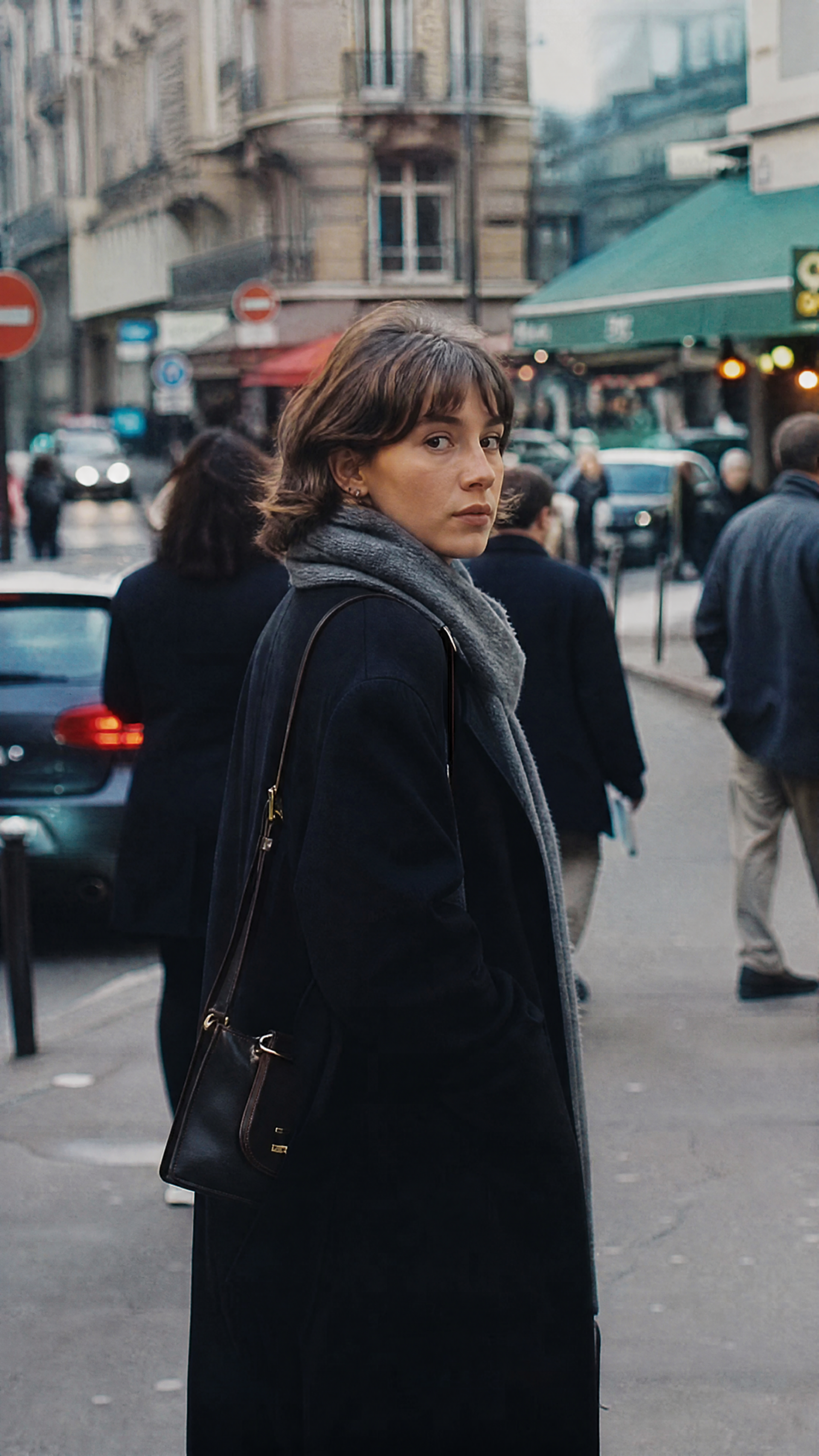 Street photography iPhone wallpaper: a woman in a dark coat and scarf looks back on a busy city street lined with cafés, cars and pedestrians.