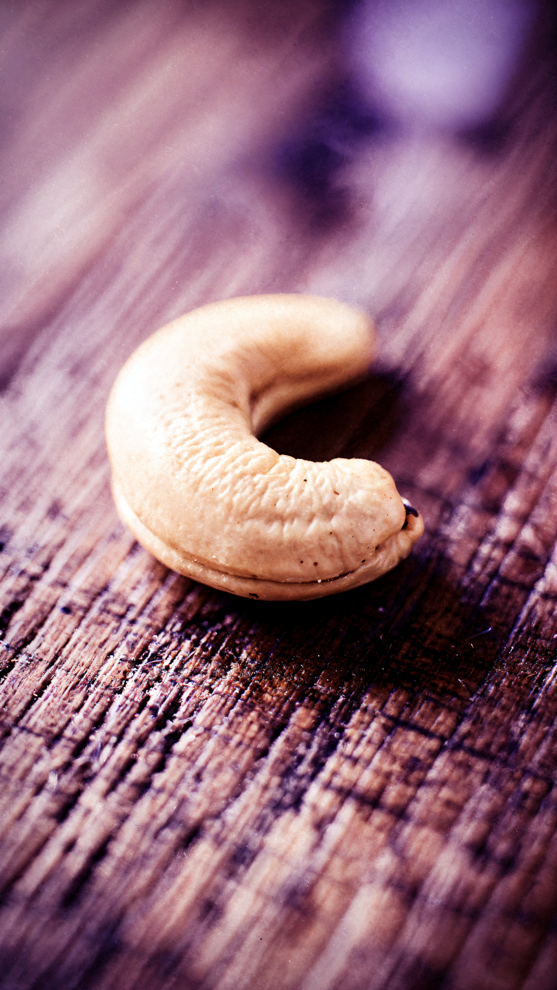 Close-up of a single cashew on weathered wood with shallow depth of field, presented in a vertical iPhone wallpaper crop.