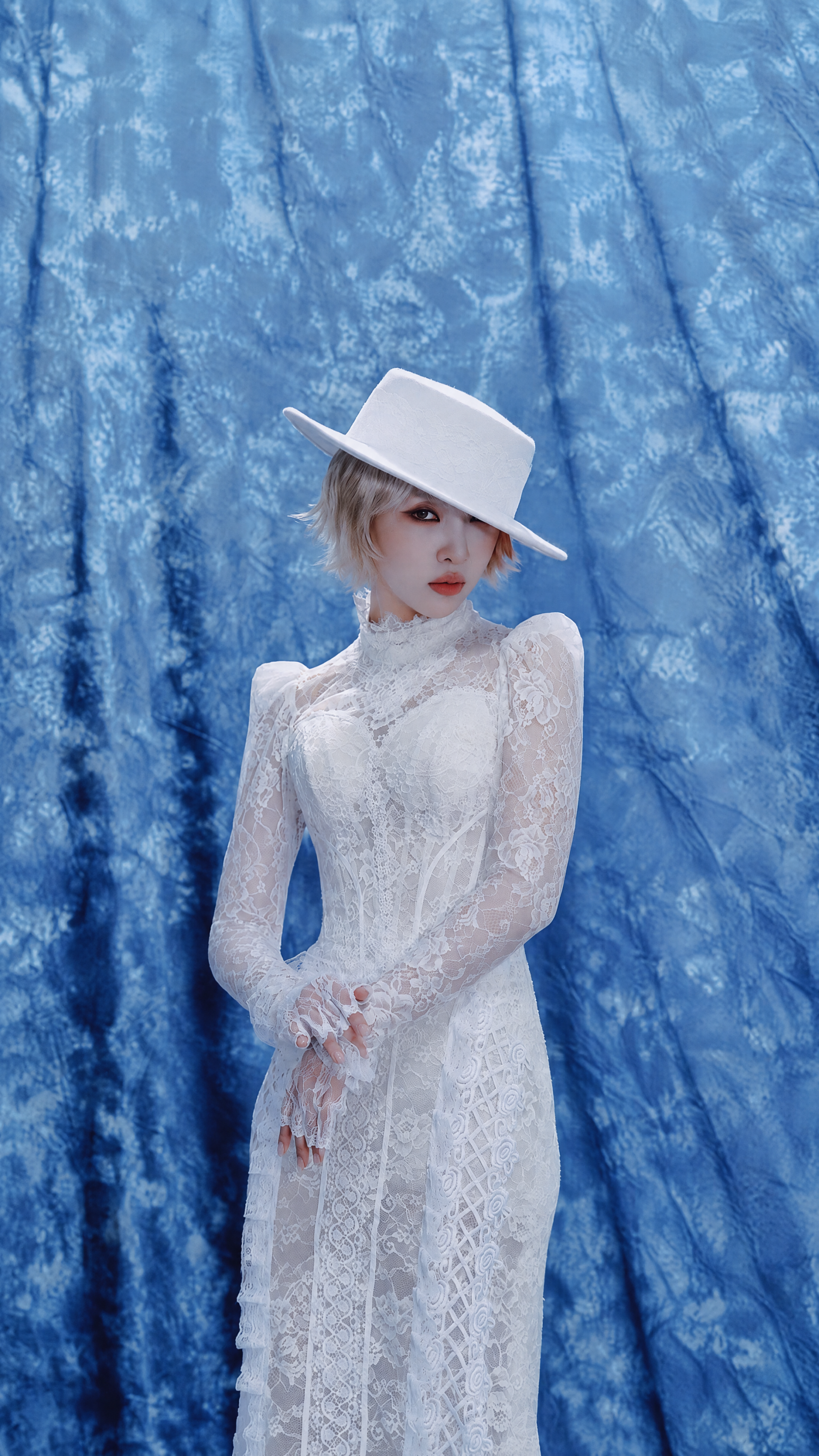 iPhone wallpaper: woman in a white lace dress and wide-brimmed white hat posed against a blue textured backdrop, styled with the word CALLING.