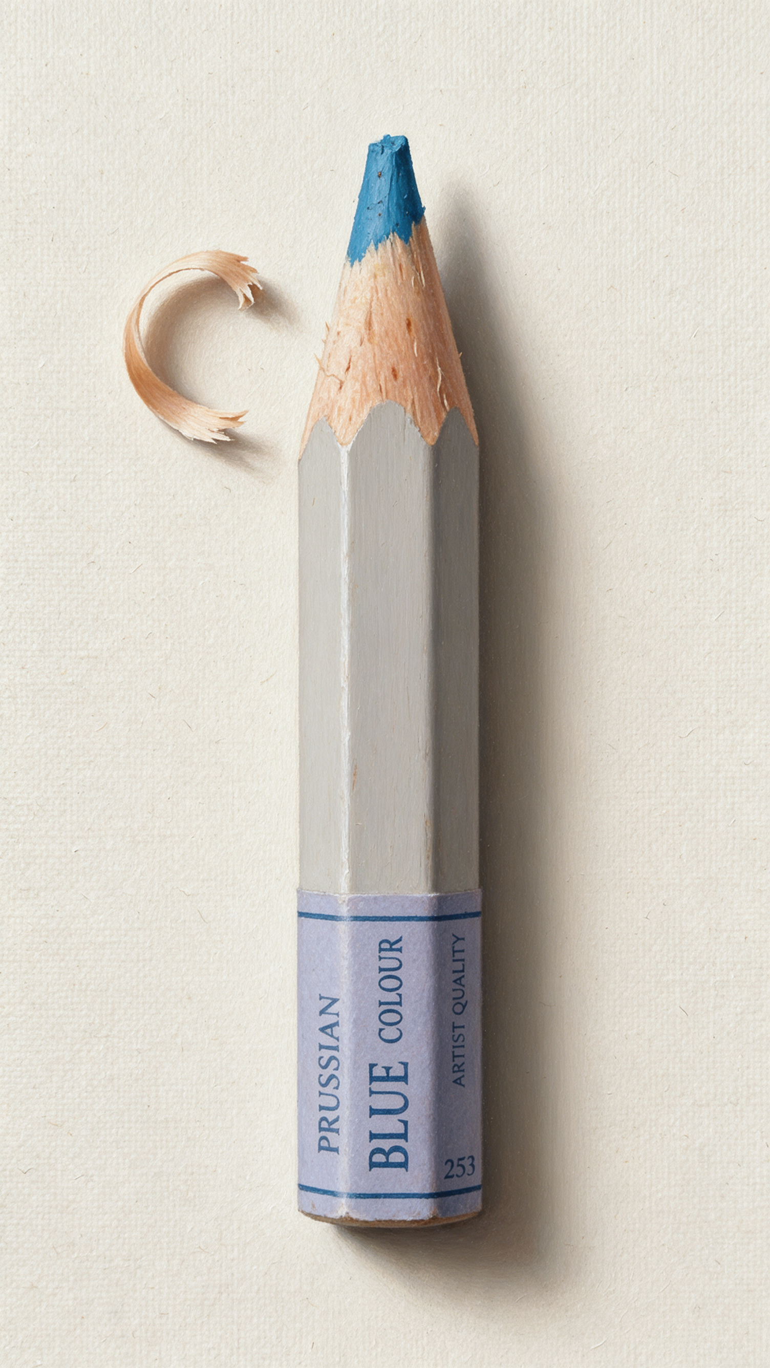 iPhone wallpaper: close-up colored pencil — a short Prussian Blue colored pencil with a sharpened blue tip and a crescent wood shaving on a pale background.