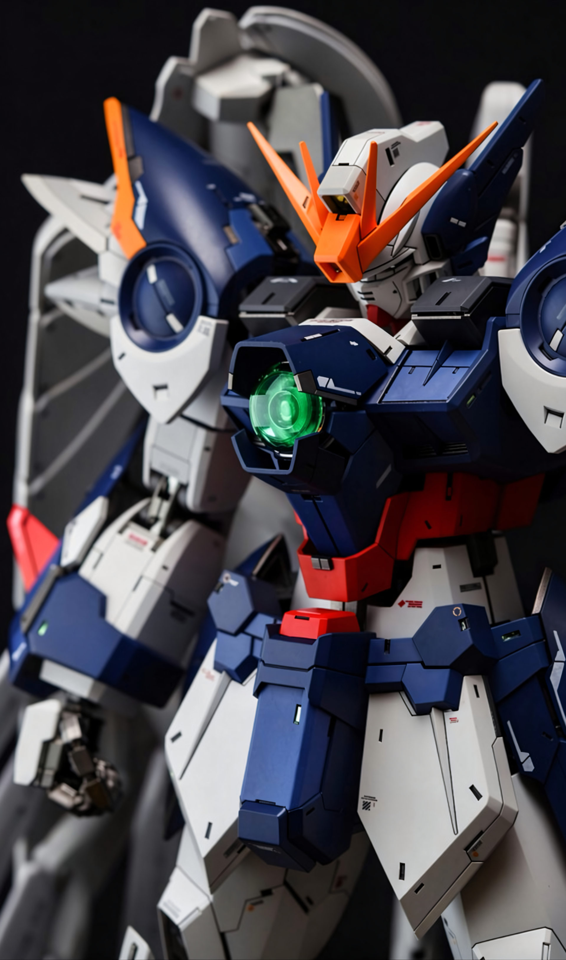 Gundam iPhone wallpaper — close-up of a detailed blue, white and orange mecha with a glowing green chest core and dramatic lighting.