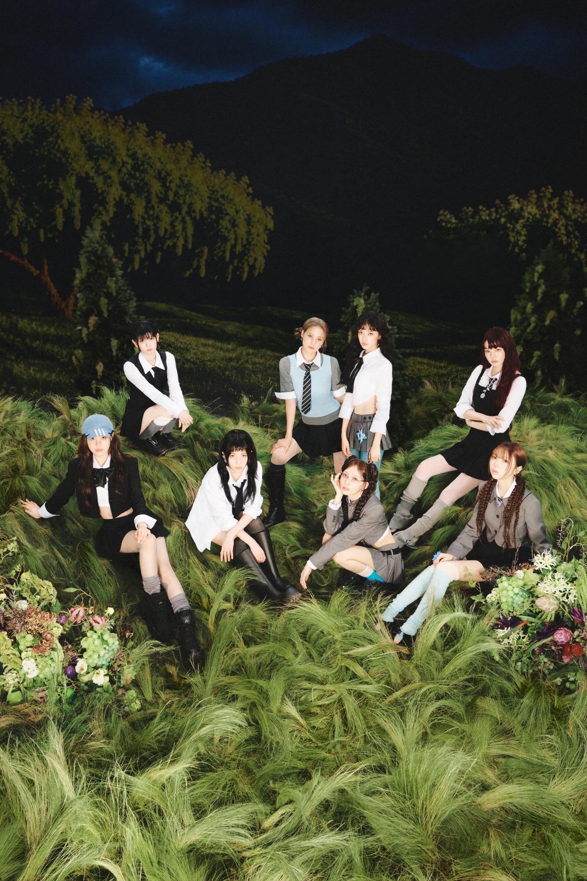 iPhone wallpaper portrait of a female pop group in a Sour Grapes concept: eight women in school-style outfits sitting on lush grass beneath a moody night sky.