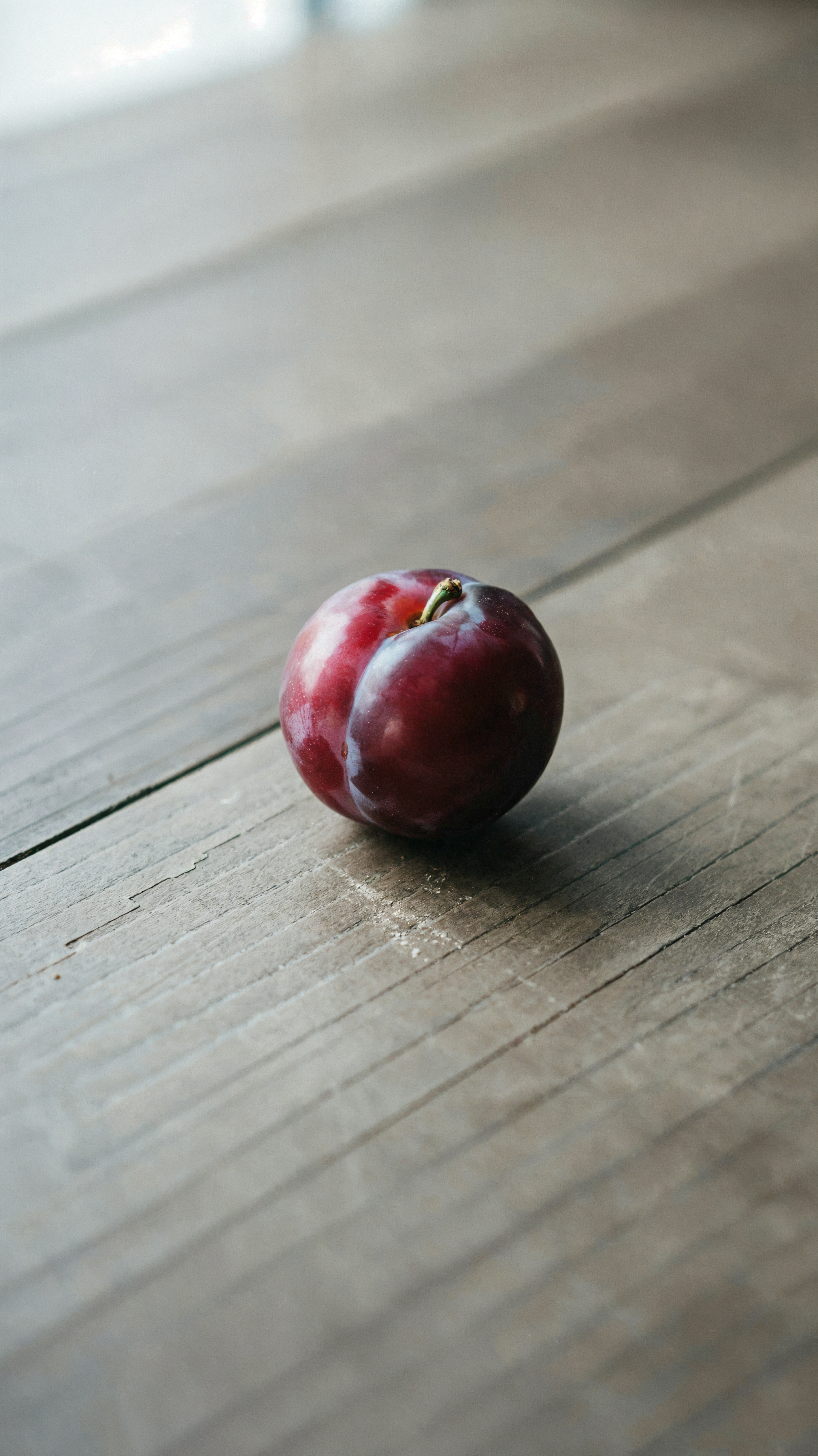 A ripe purple plum on a rustic wooden table, minimalist iPhone wallpaper.