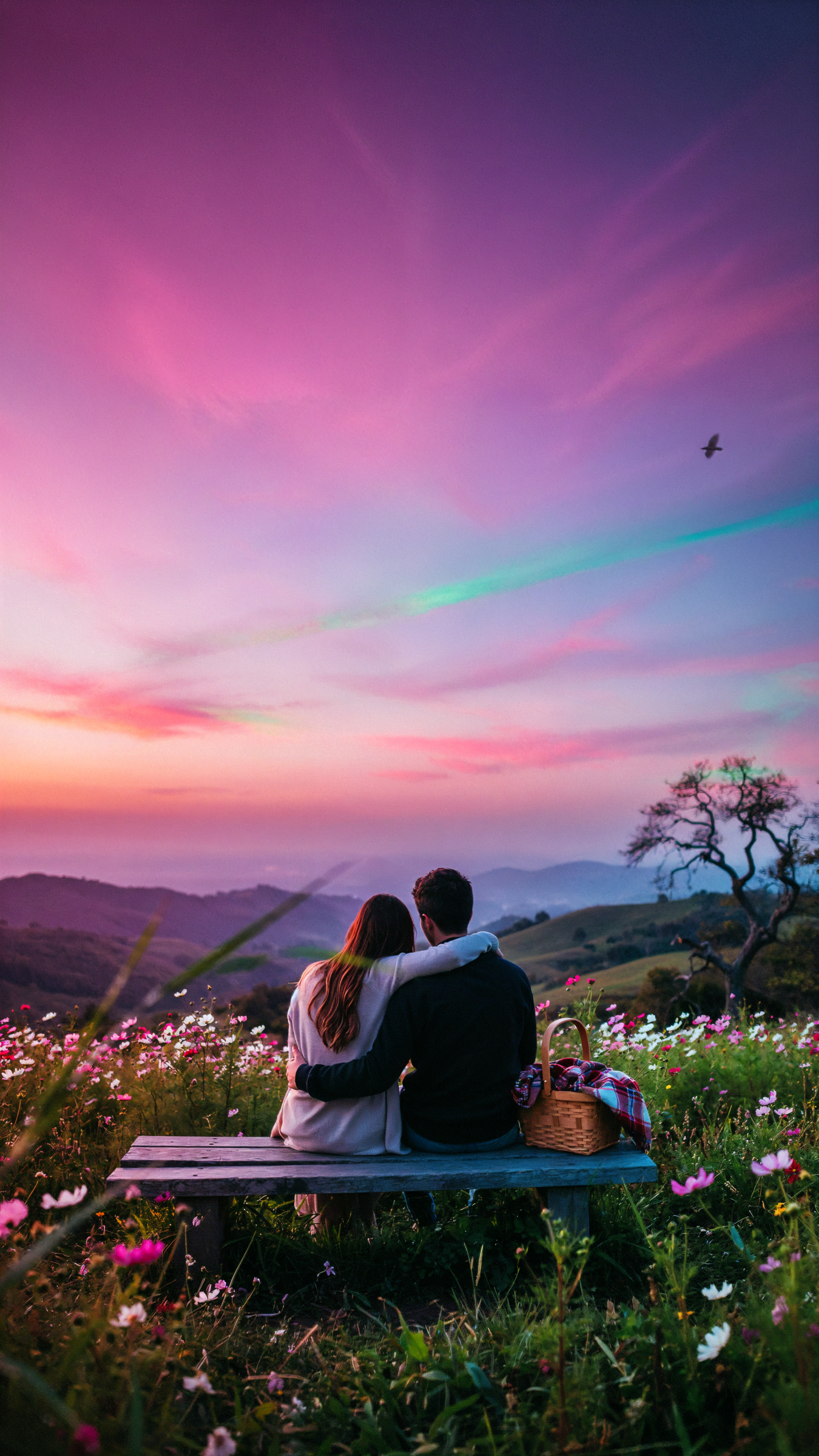 Romantic couple sitting in a flower-filled meadow beneath a vivid pink sunset, scenic iPhone wallpaper.