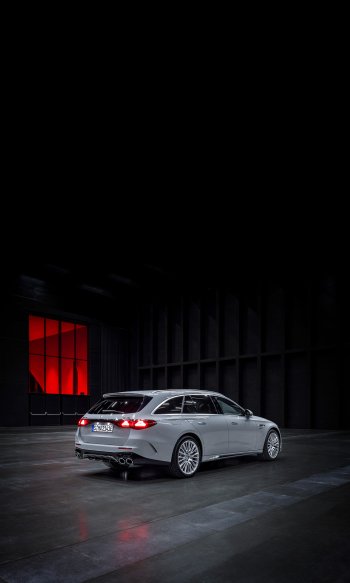 A sleek Mercedes-AMG E 53 Hybrid is parked in a dramatic, dimly lit space, showcasing its stylish design against a backdrop of striking red lighting.