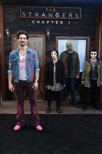 Phone wallpaper featuring characters from the movie The Strangers: Chapter 1 standing in front of a wooden house with The Strangers Chapter 1 sign above.