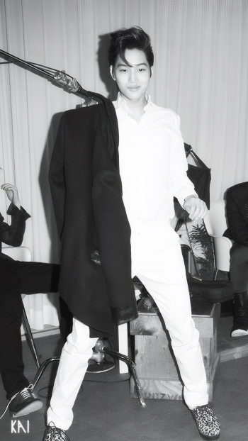 Black-and-white phone wallpaper of EXO’s Kai in a photoshoot for MAMA, dressed in white with a jacket slung over his shoulder, set against a studio backdrop.