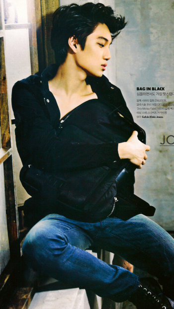 Side-profile of a young male model in a GQ magazine photoshoot, clutching a black jacket while seated against a textured wall — phone wallpaper sized for iPhone and Android.