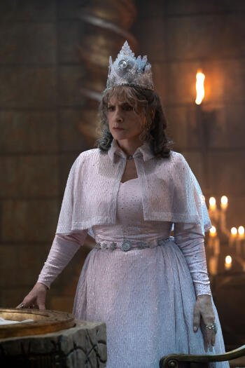 A scene from the TV show Agatha All Along, featuring a character in a regal outfit and crown, standing in a dimly lit room with candles, creating an intriguing atmosphere.