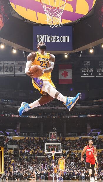 LeBron James soars in a dynamic moment during a Lakers game, showcasing his skills on the court with vibrant team colors and a packed arena in the background. Perfect NBA wallpaper.