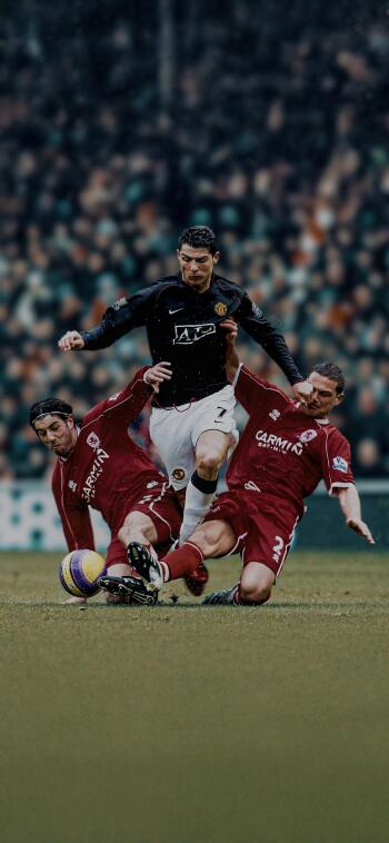 Cristiano Ronaldo, wearing Manchester United F.C. colors, skillfully maneuvers past two opponents during a dynamic soccer match. A striking phone wallpaper for fans.