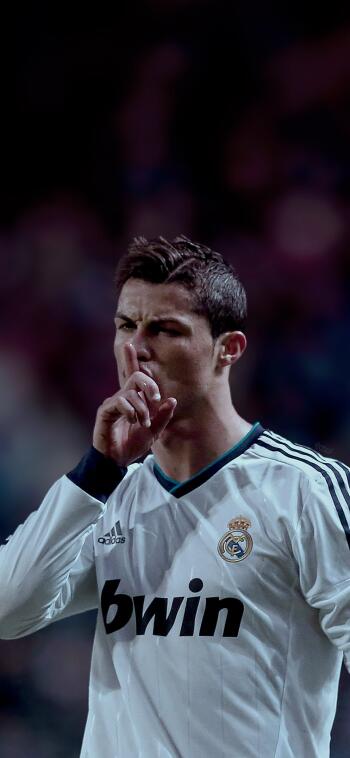 Cristiano Ronaldo poses in a Real Madrid C.F. jersey, gesturing for silence amidst a vibrant stadium backdrop, capturing the intensity of the sport. Perfect for soccer fans.