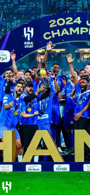 Celebrating their victory, the Al Hilal SFC players joyfully lift the championship trophy in their blue jerseys, surrounded by confetti and a banner that reads 2024 Champions.