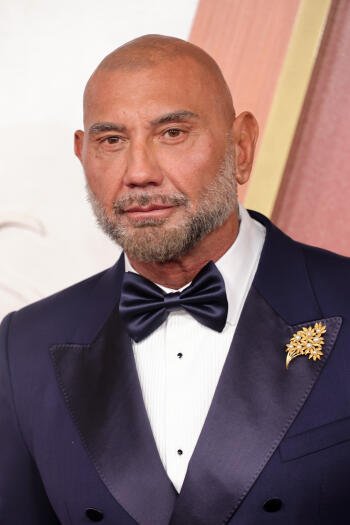 A dapper Dave Bautista in a formal black tuxedo with a bow tie and a decorative lapel pin, captured at the Academy Awards, serves as an impressive phone wallpaper.