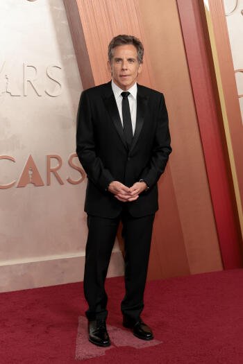 Ben Stiller in a black tuxedo stands on the red carpet at the Academy Awards, exuding elegance and charm against the iconic Oscars backdrop.