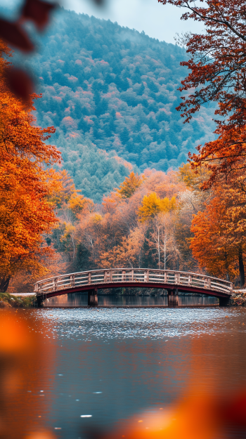 A serene autumn scene featuring a wooden bridge over a calm river, surrounded by vibrant fall foliage and distant mountains, creating a tranquil phone wallpaper.
