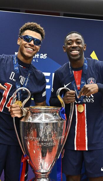 Ousmane Dembélé and Désiré Doué of Paris Saint-Germain smile while holding the UEFA Champions League trophy, captured in a vibrant soccer-themed phone wallpaper.